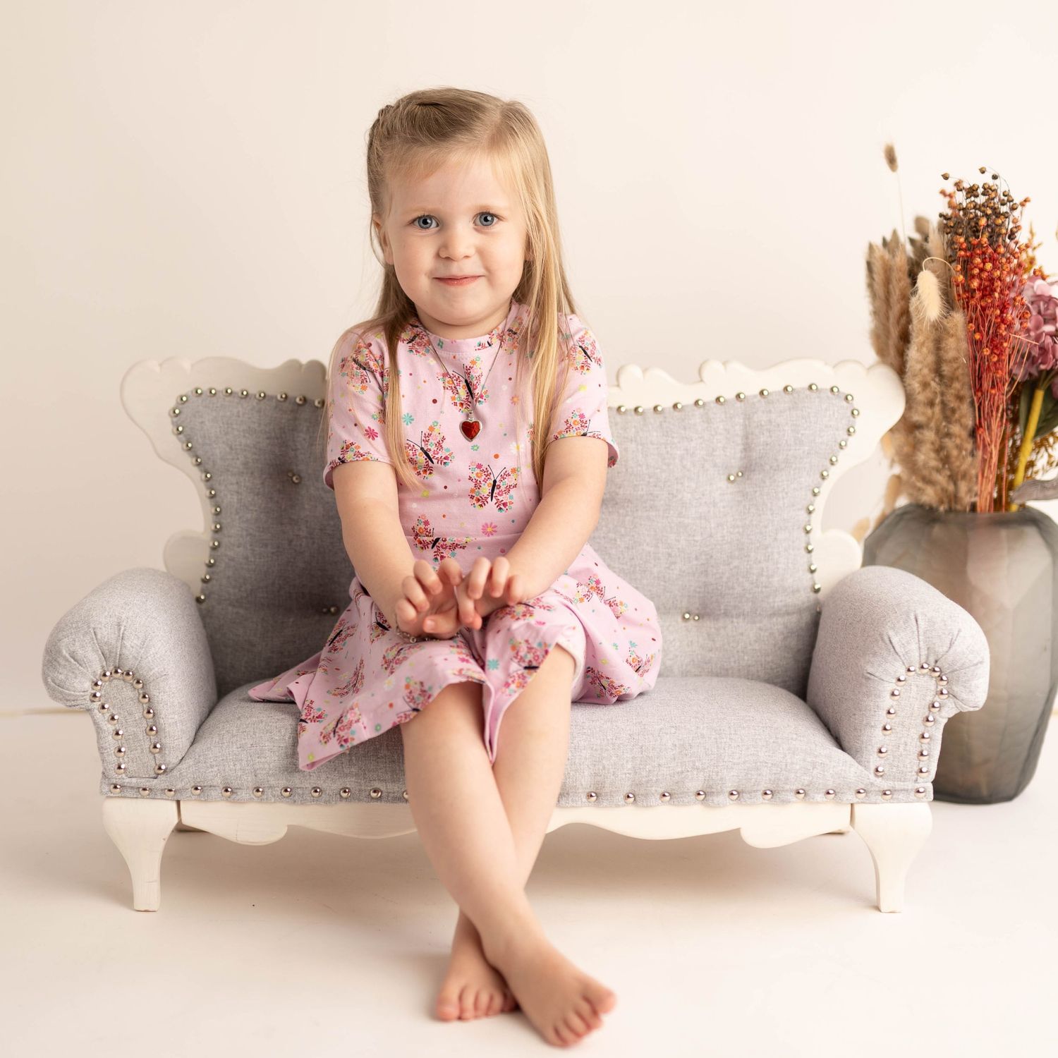 Elegant studio photo on grey tufted loveseat with pink floral dress.