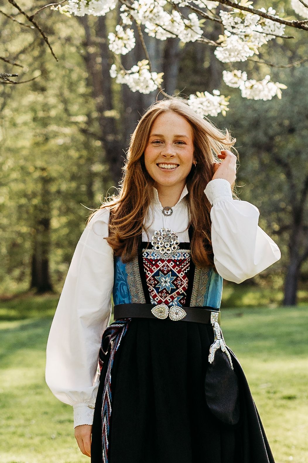 Folk dress with ornate embroidery photographed under blooming spring trees.