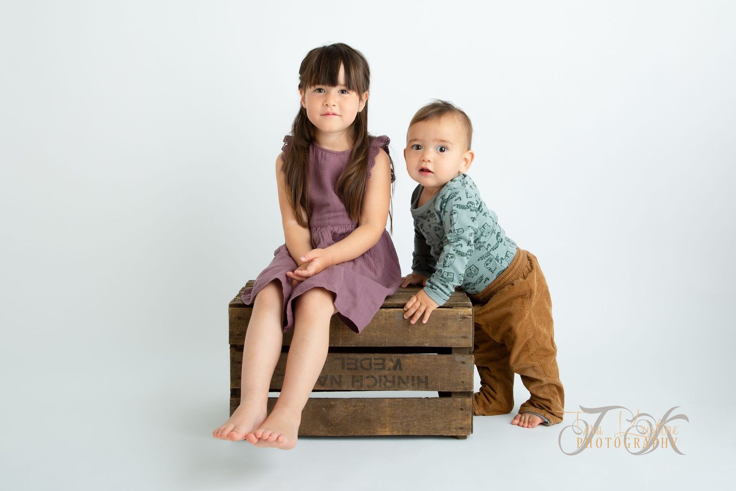 Studio portraits of siblings interacting with vintage wooden crate against white background.