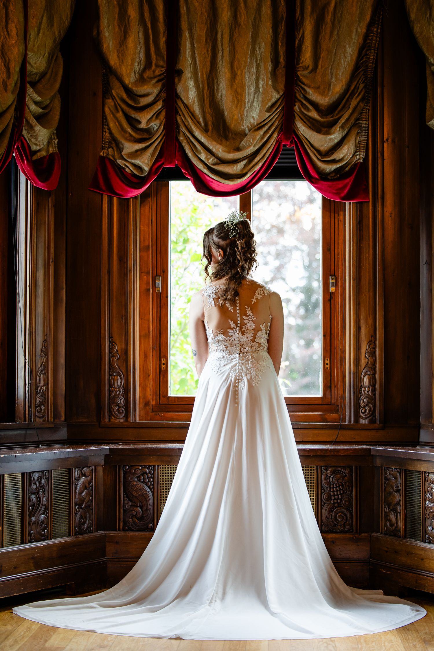 A flowing white wedding gown with lace details displayed in an ornate wood-paneled room.