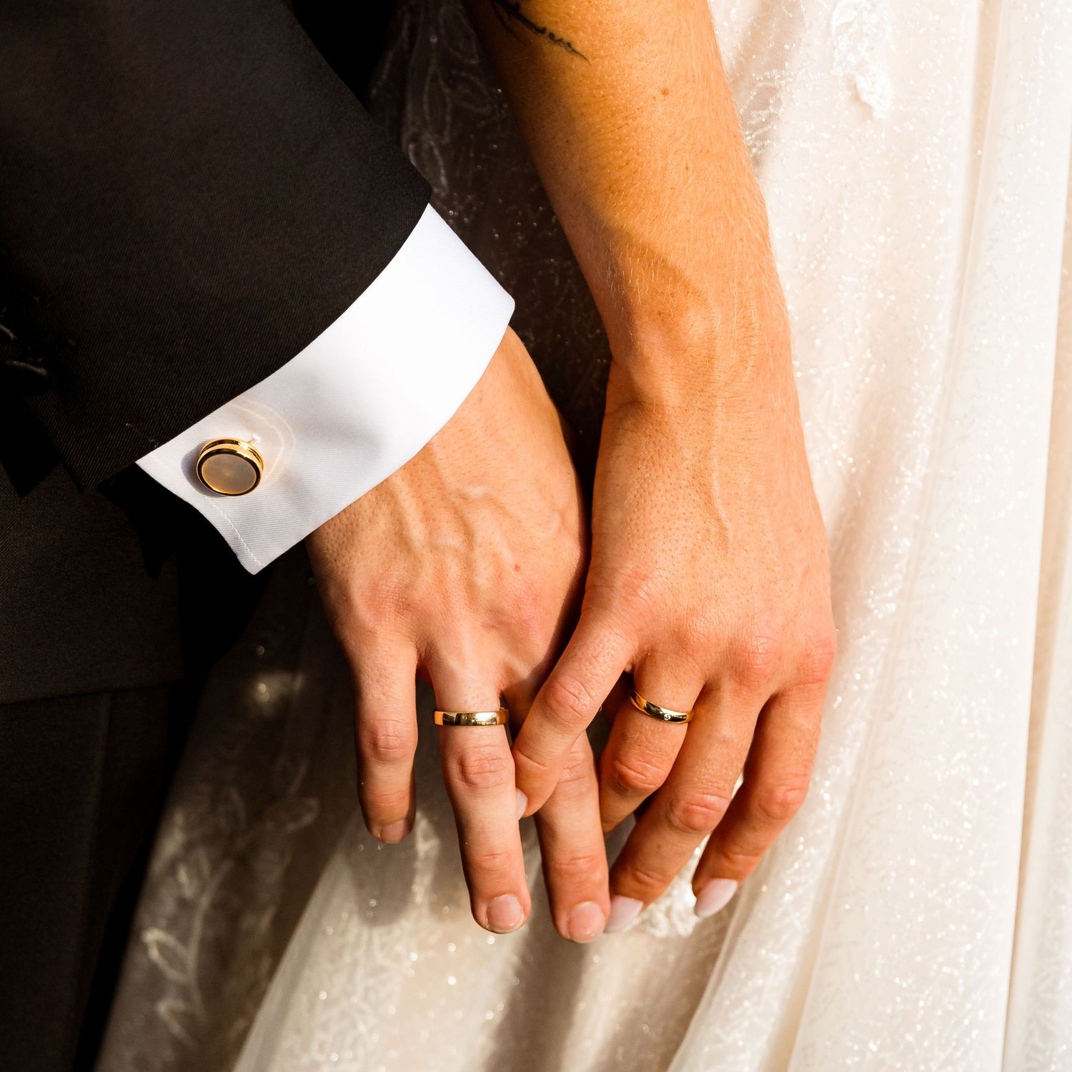 Close-up shot of wedding rings and hands against white fabric.