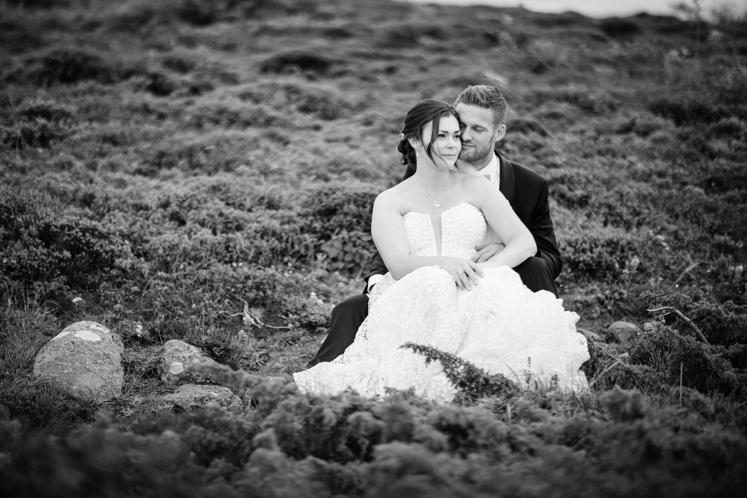 A couple sits together on a grassy hillside in black and white photography.