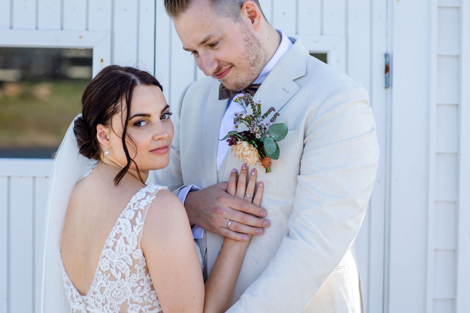 Romantic wedding couple embraces against white wooden backdrop in soft natural lighting.