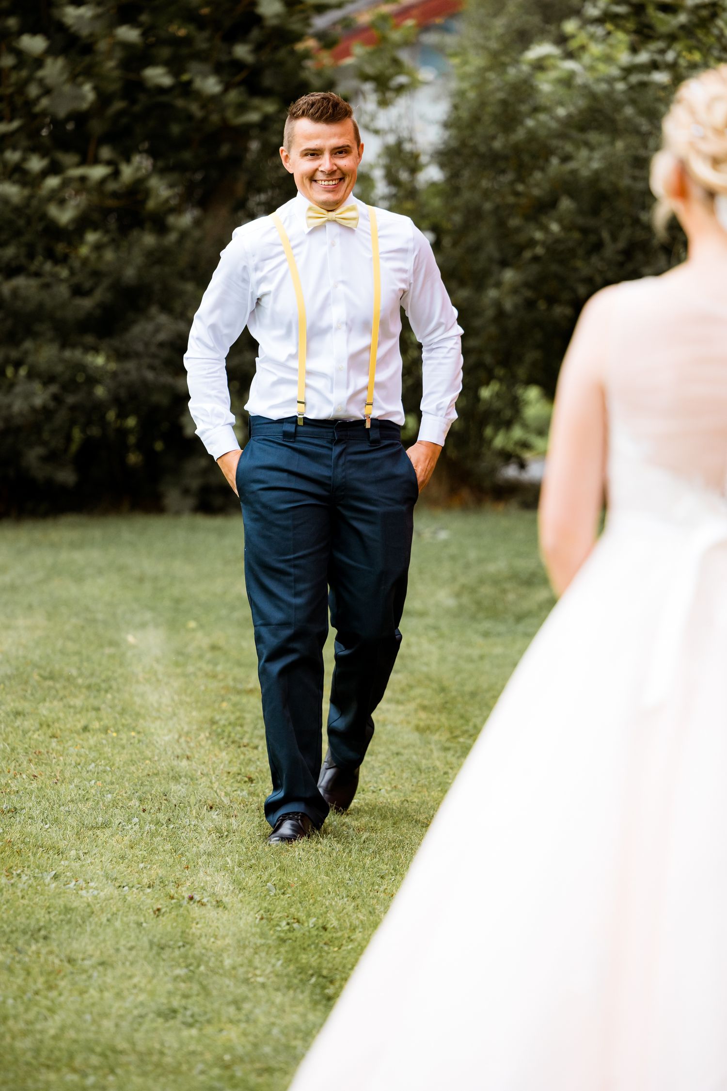 Playful first look moment in garden with groom wearing suspenders and yellow bow tie.