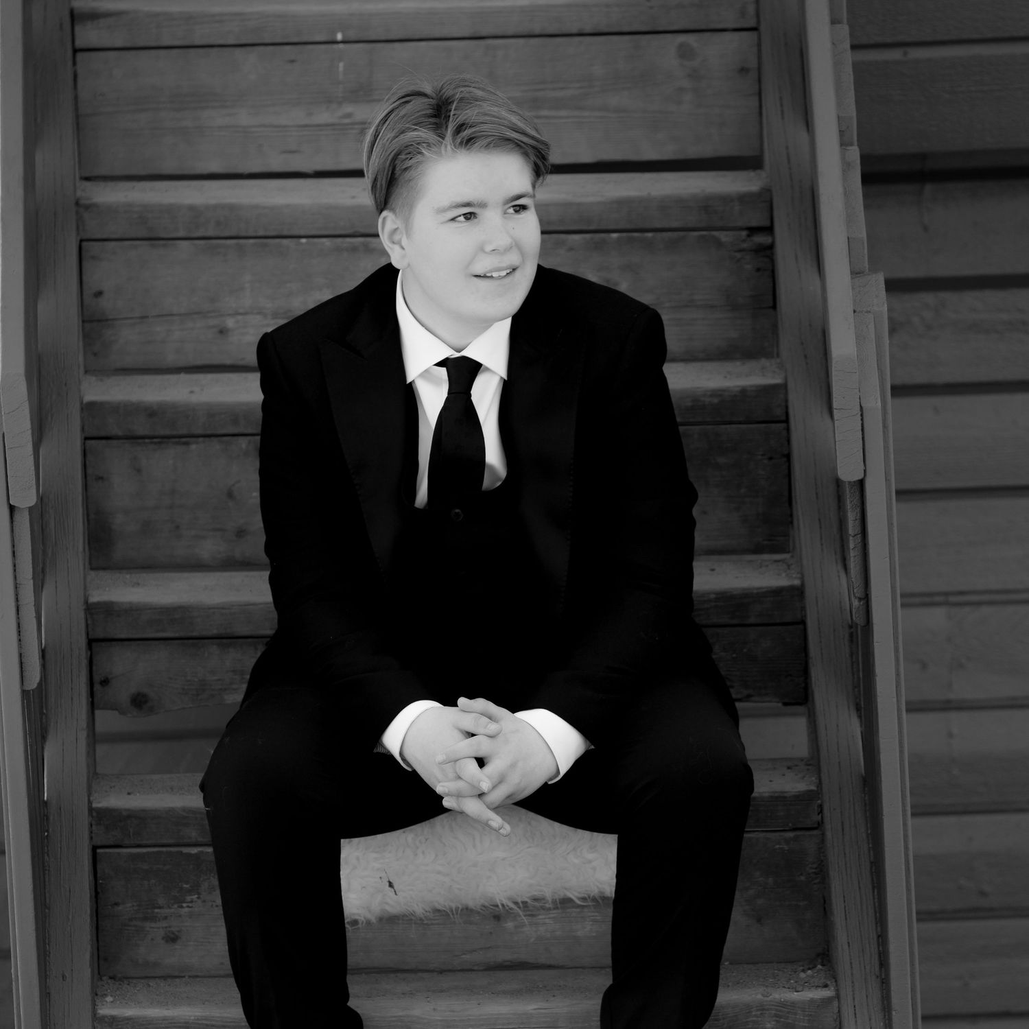 Black and white portrait of person in formal suit sitting on wooden steps.
