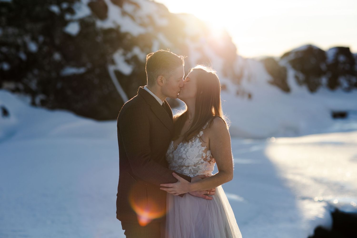 Sunlit winter wedding portrait with snow covered landscape in background.