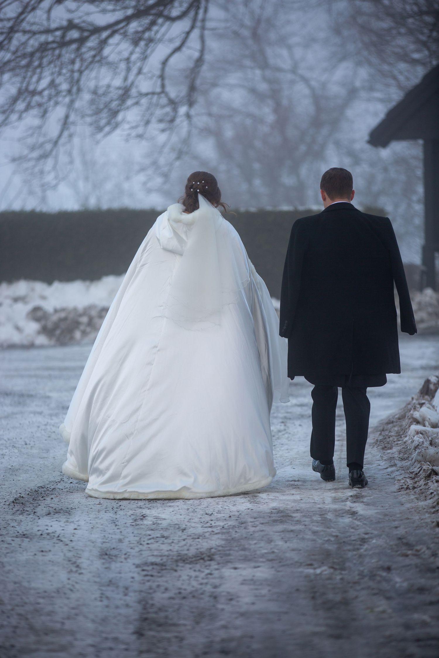 A couple walking in the snow with the bride's white dress trailing behind them.