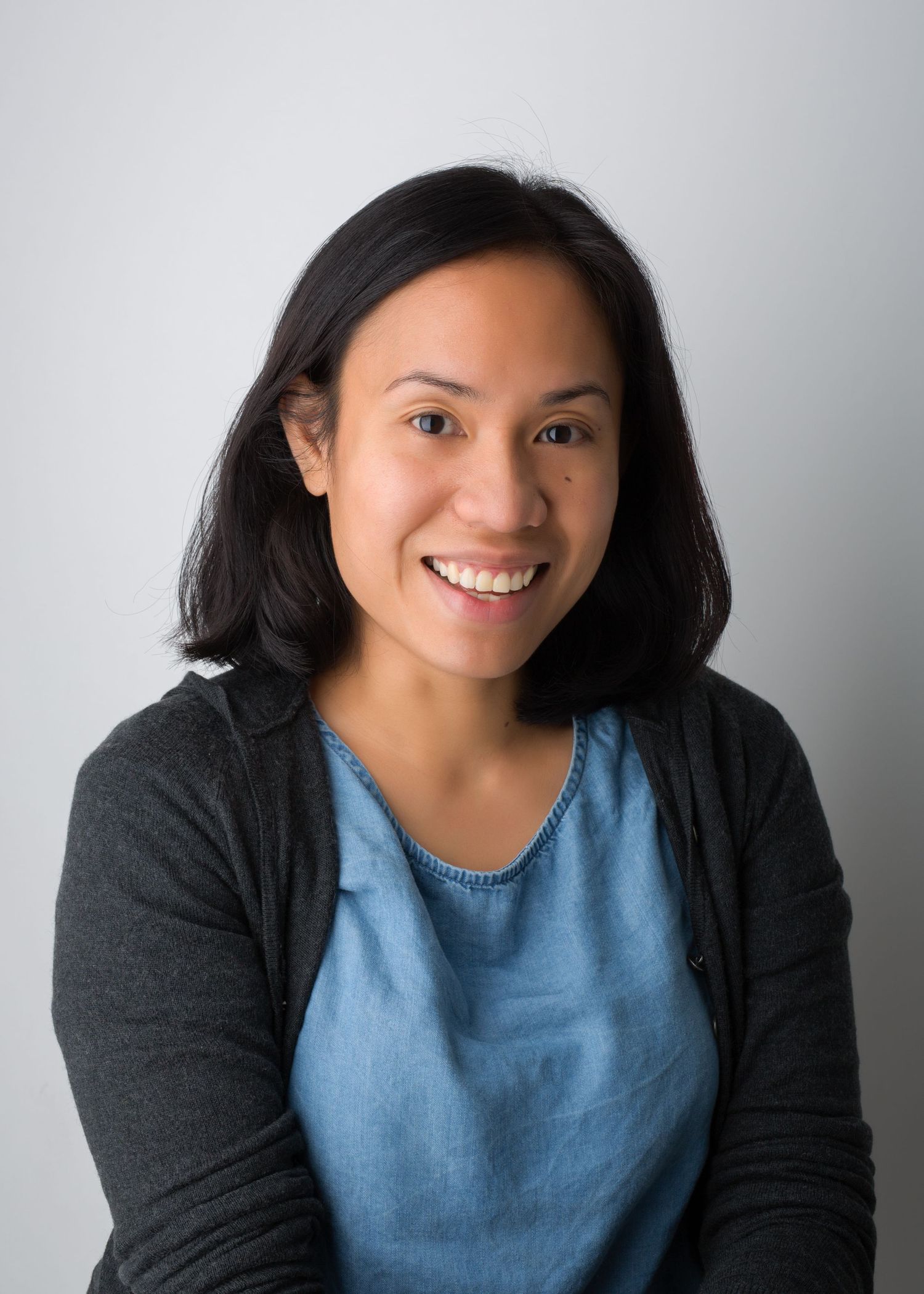 Professional headshot of person in dark cardigan and blue top against light background.