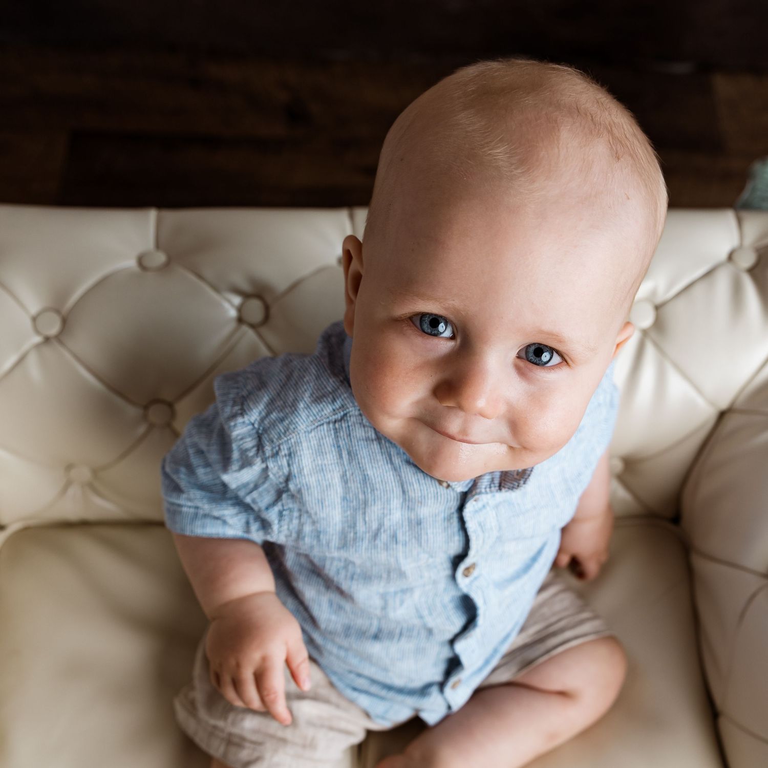 Baby in light blue outfit resting on white tufted couch during portrait session.