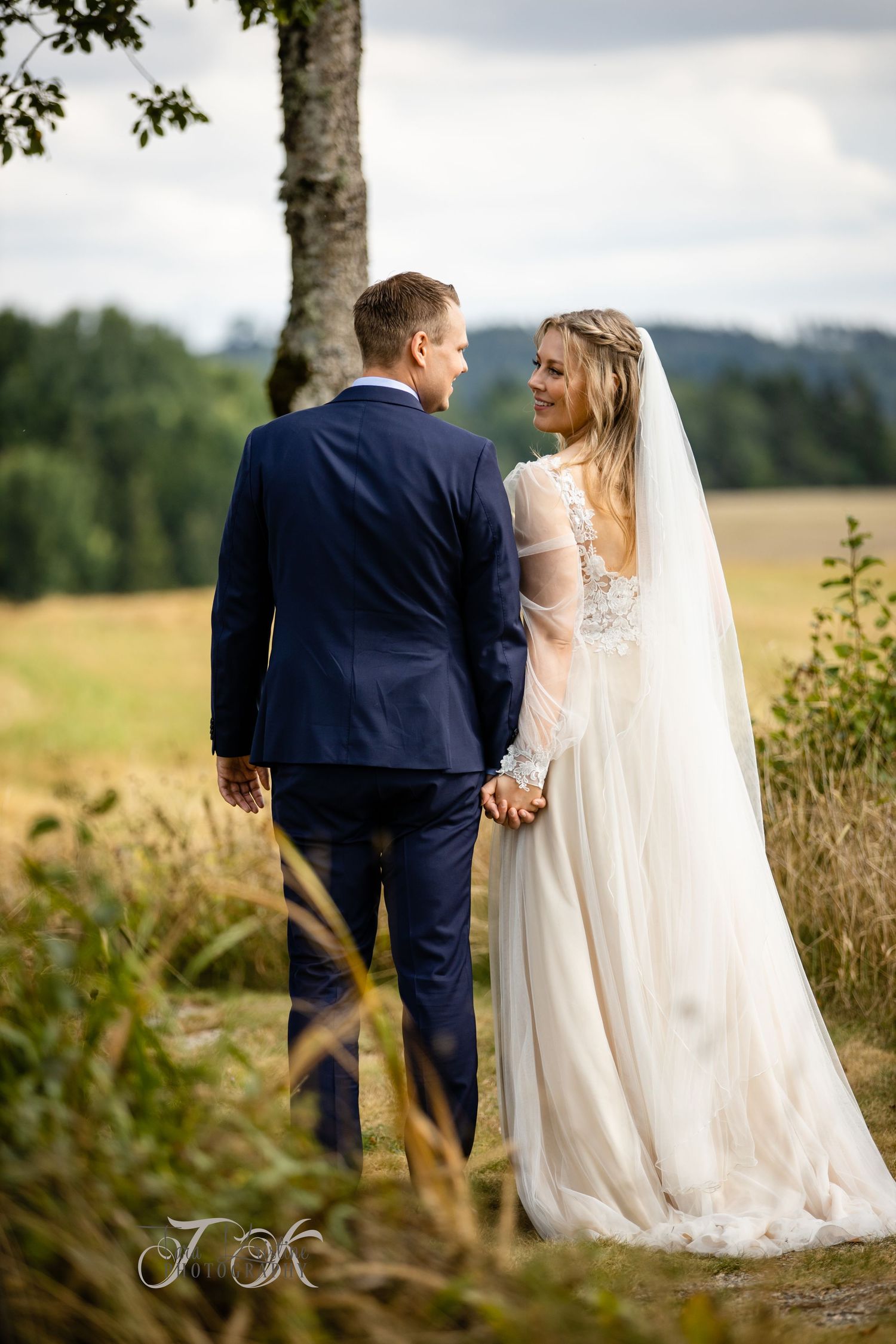 A couple walks hand in hand through a meadow on their wedding day.