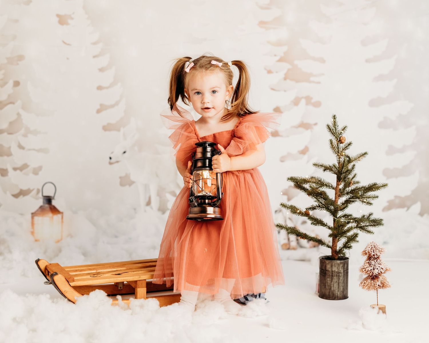 A child in a peach tulle dress poses with vintage Christmas decorations against a white backdrop.