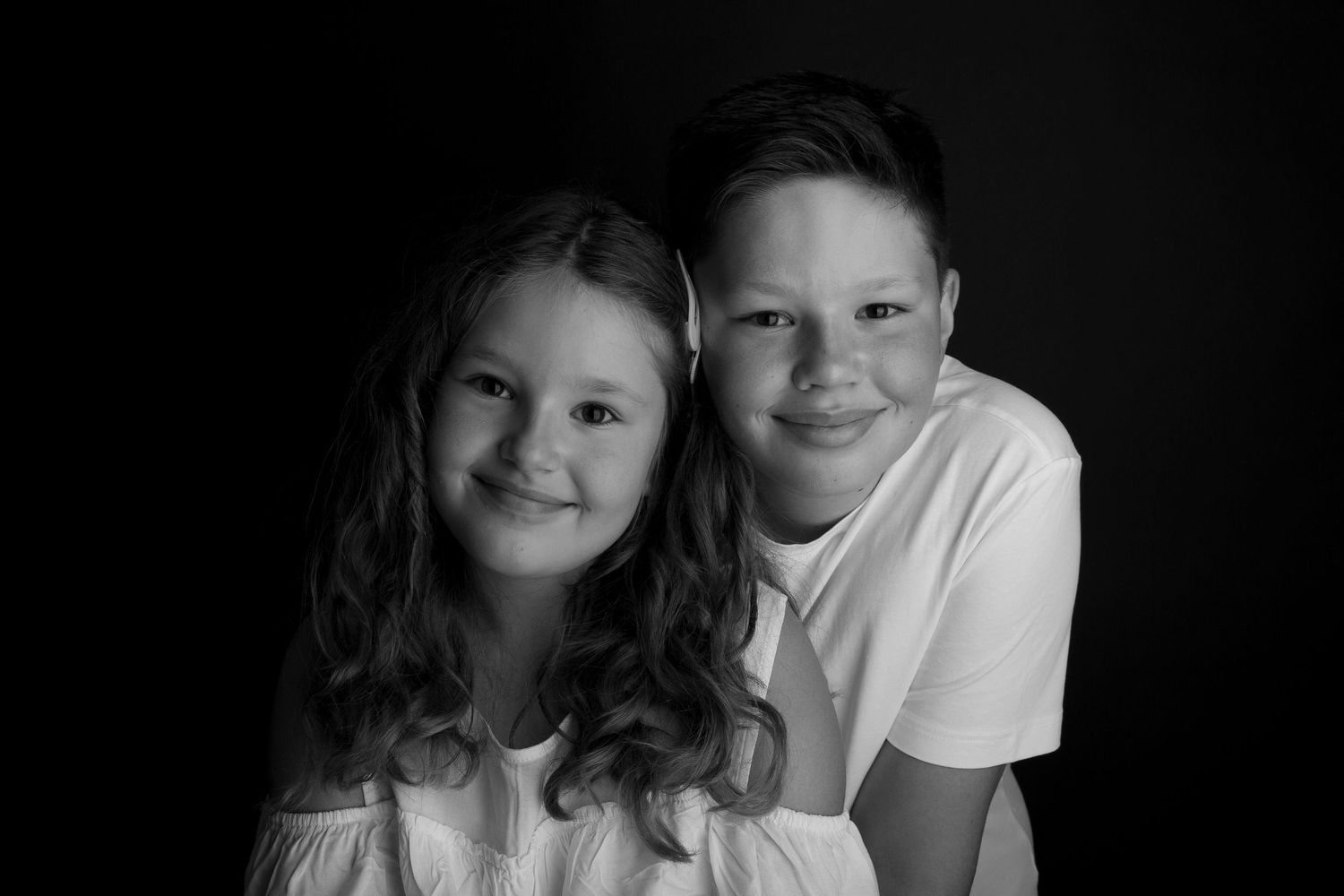 Black and white studio portraits of siblings sharing playful moments together.