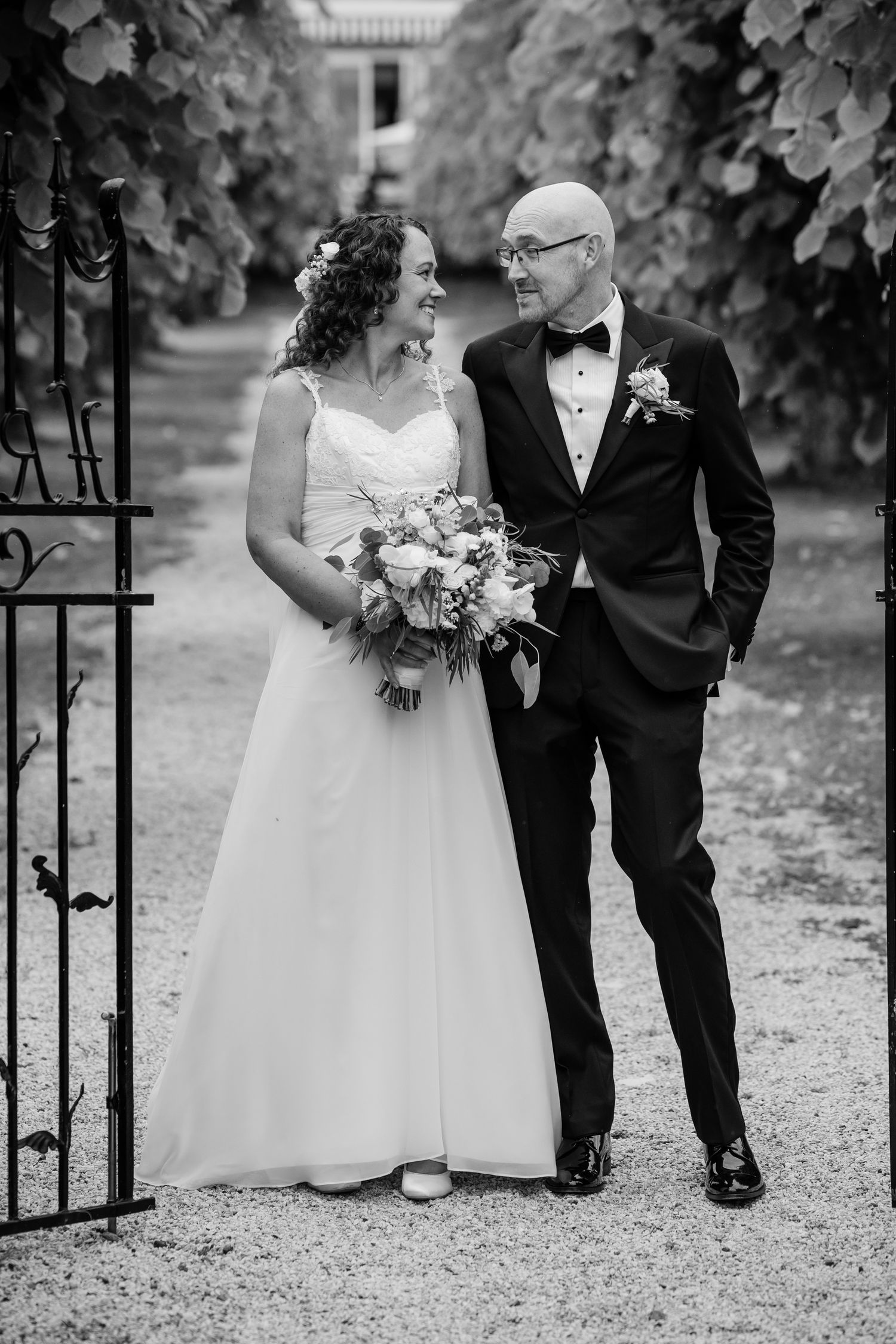 Wedding couple walking along a garden path with decorative iron gates.