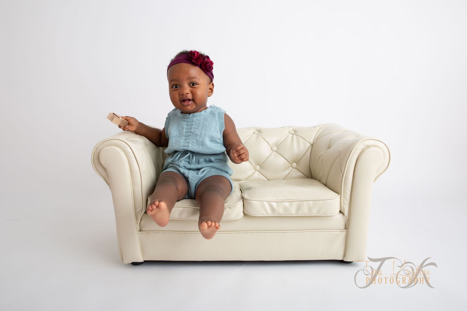 Ettårsfotografering Moss: En blid baby sitter på en liten, hvit chesterfield-sofa i fotostudioet i Våler.