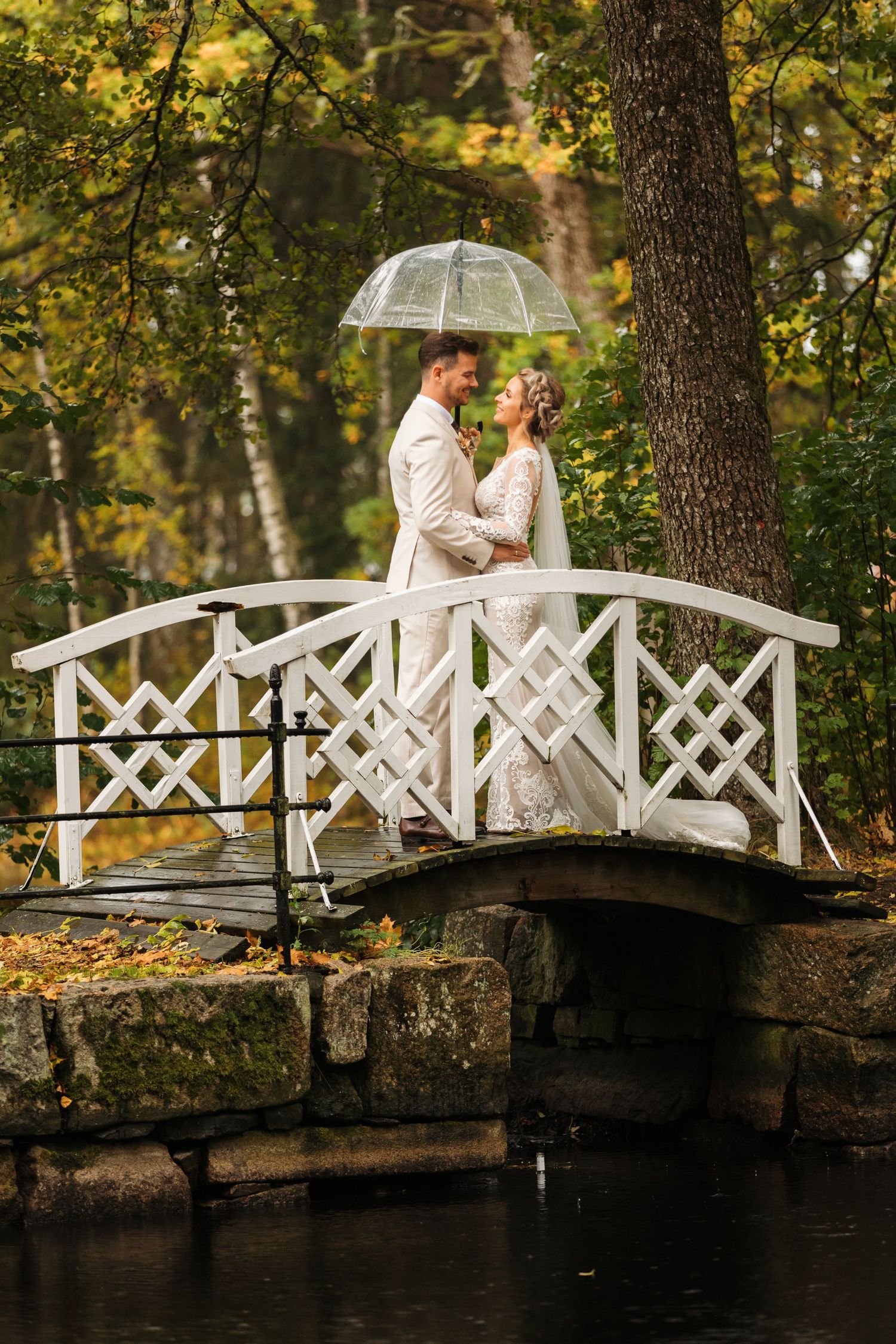 Romantic couple sharing an intimate moment on a white wooden bridge in an autumn park setting.