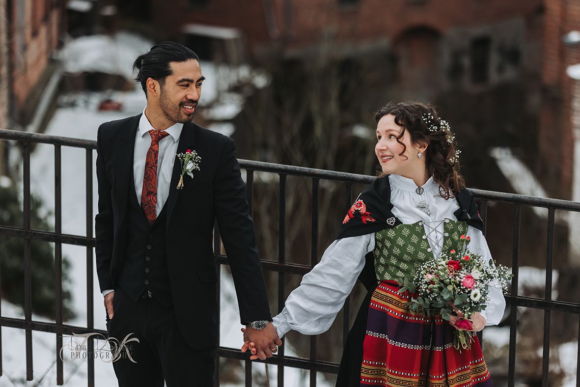 A couple shares a romantic moment in winter wedding attire near brick architecture.
