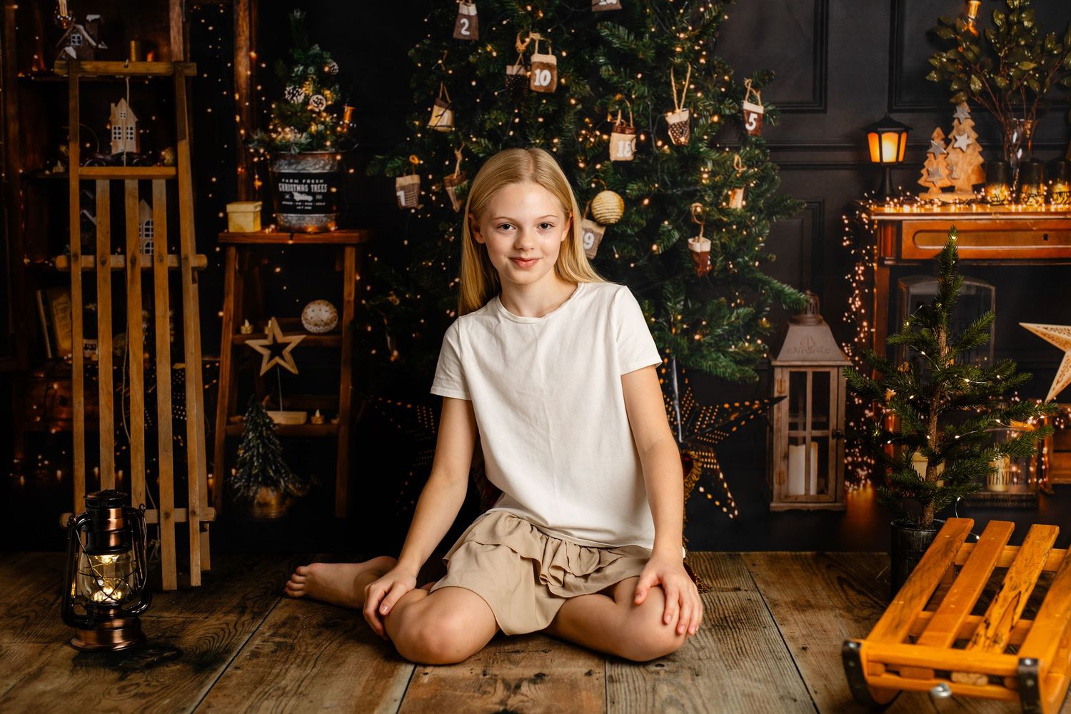 Festive Christmas photo session setup with wooden sleigh and decorated tree in background.