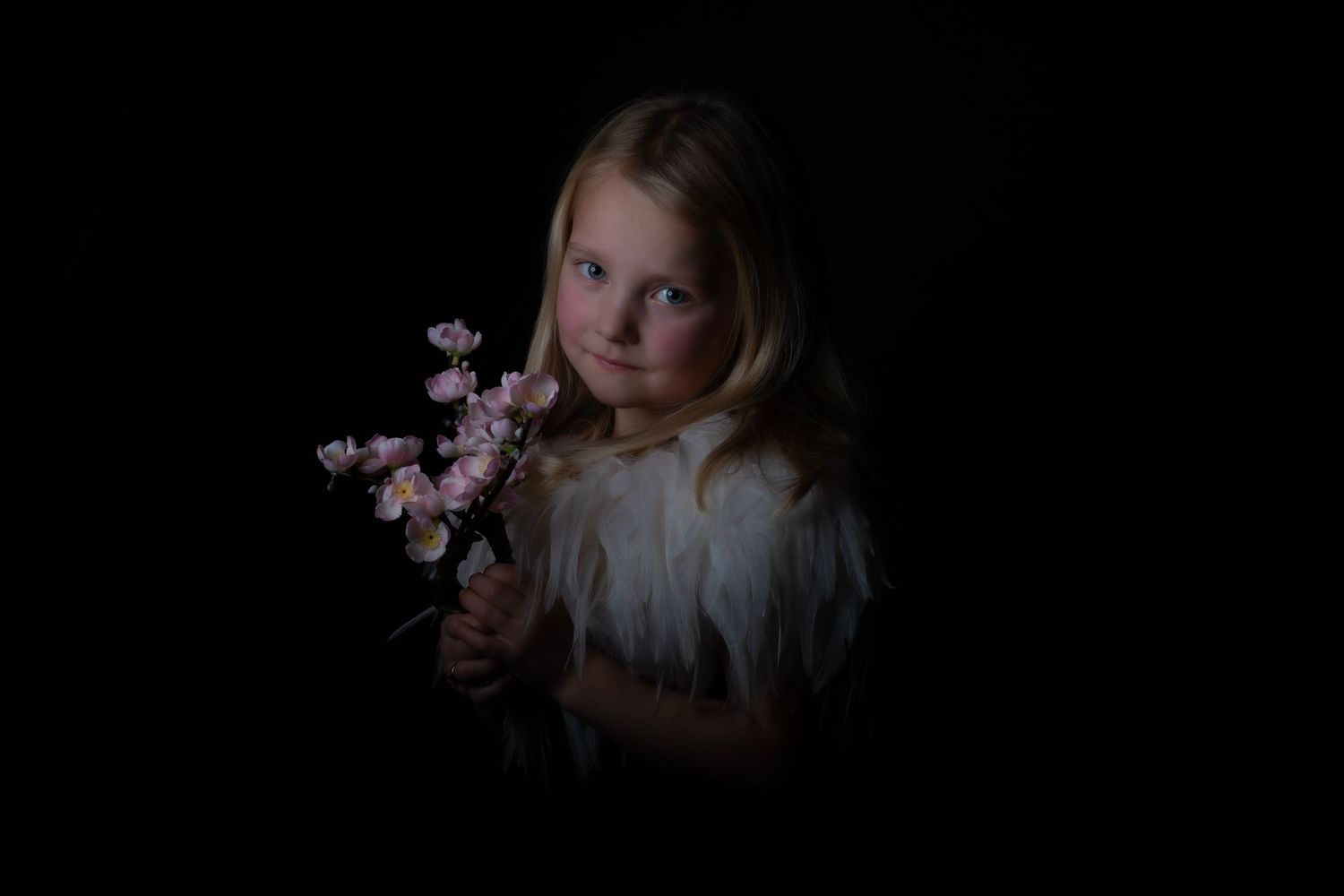 Dramatic low-key portrait holding pink flowers against dark background.