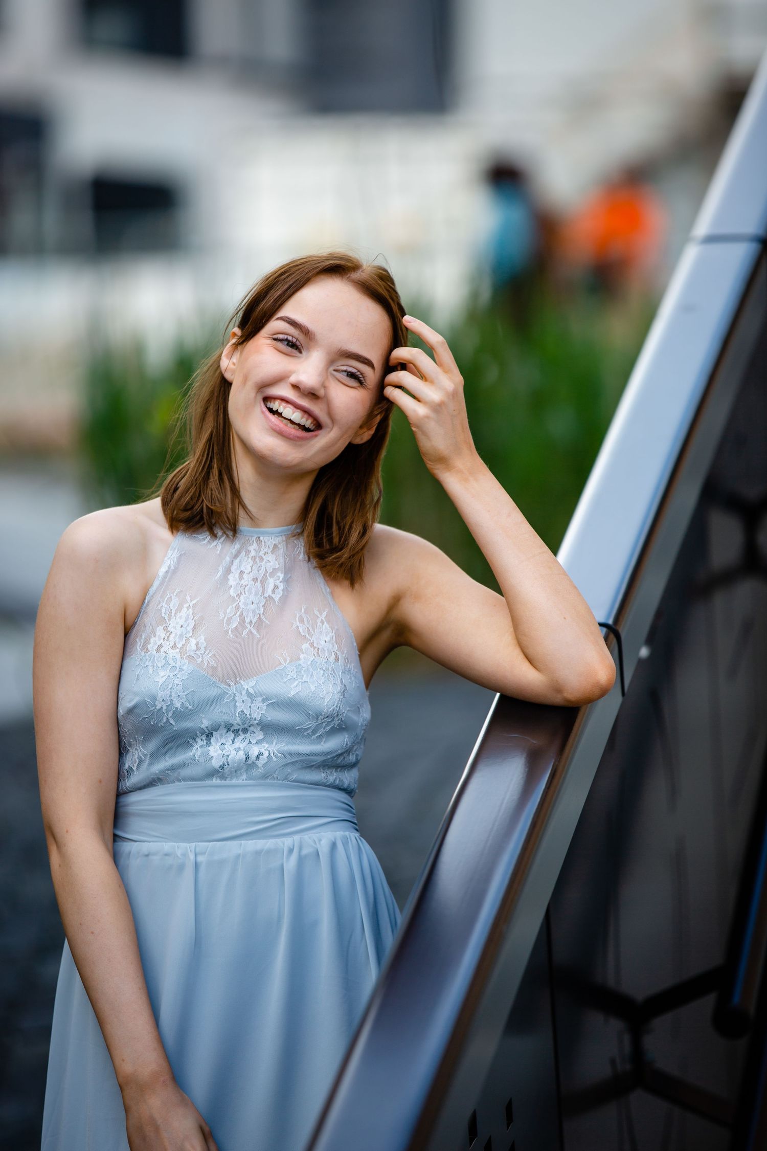 A joyful portrait of someone in a pale blue dress with lace details leaning against a wall outdoors.