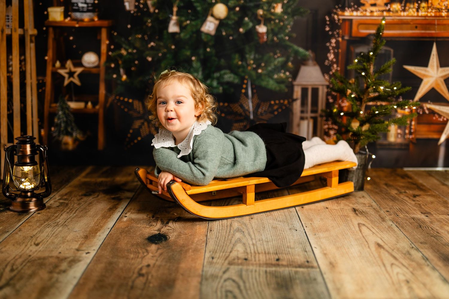 Playful holiday scene with wooden sled against decorated Christmas tree background.