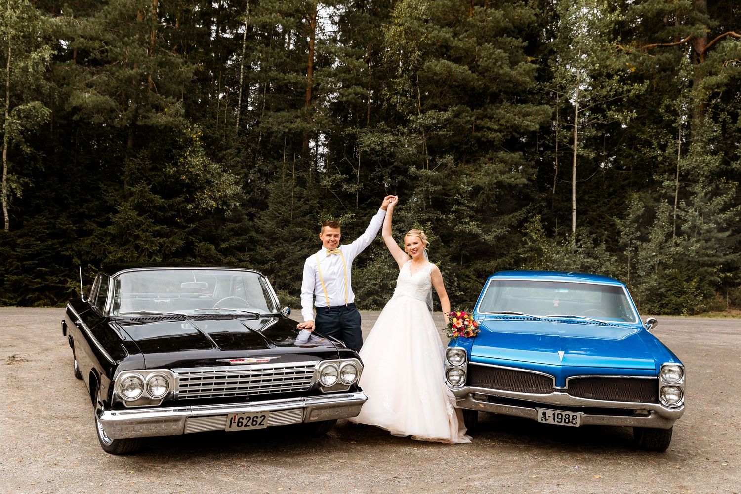 Wedding couple posing between vintage black and blue classic cars.