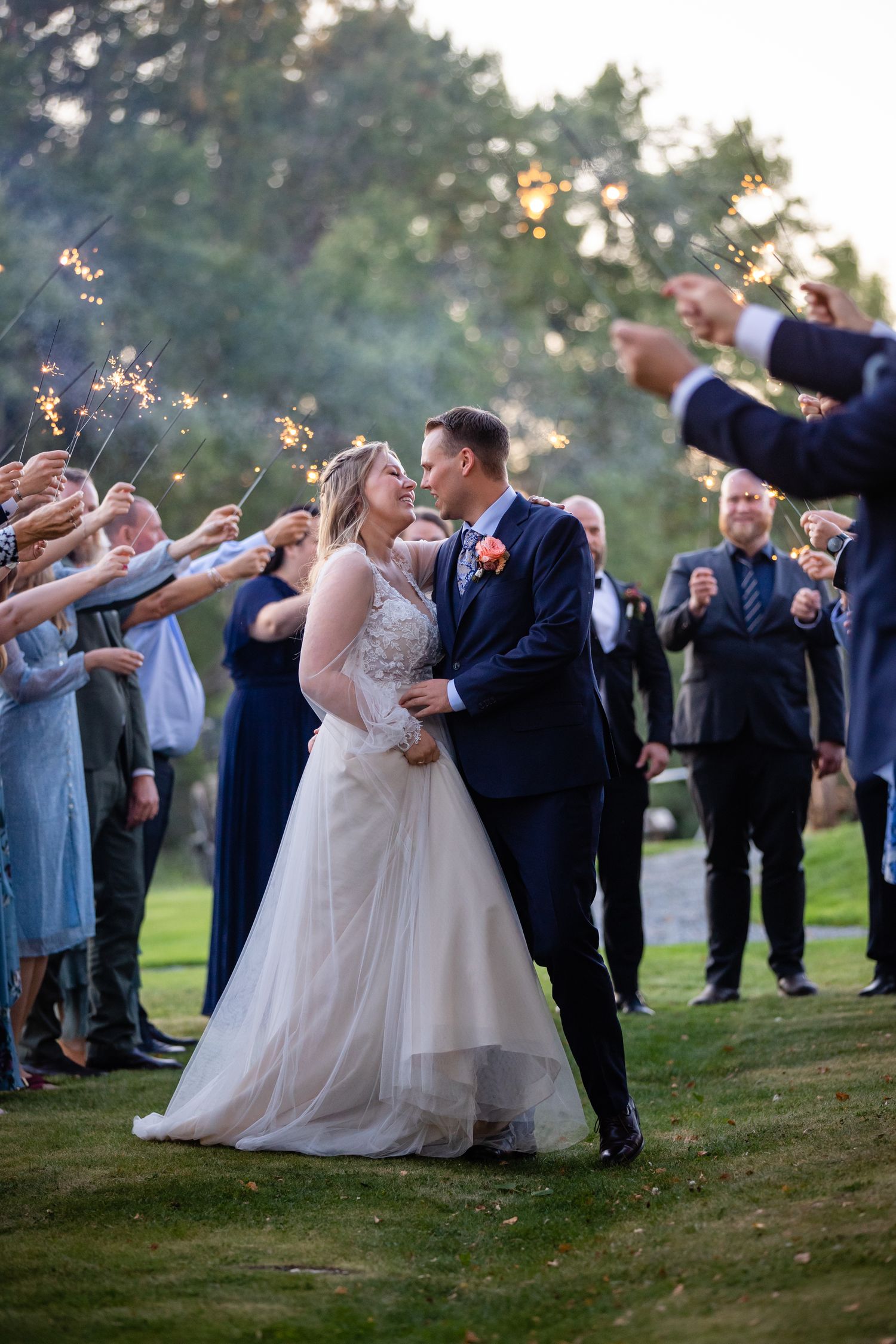 Wedding party celebrating with sparklers at twilight on a grassy hillside.