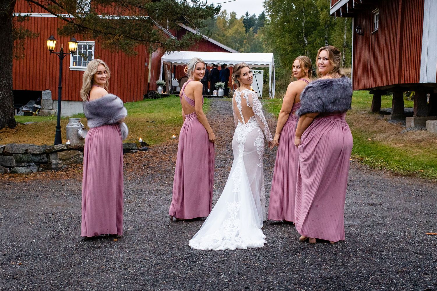Wedding party in pink dresses poses outside red barn in rustic setting.