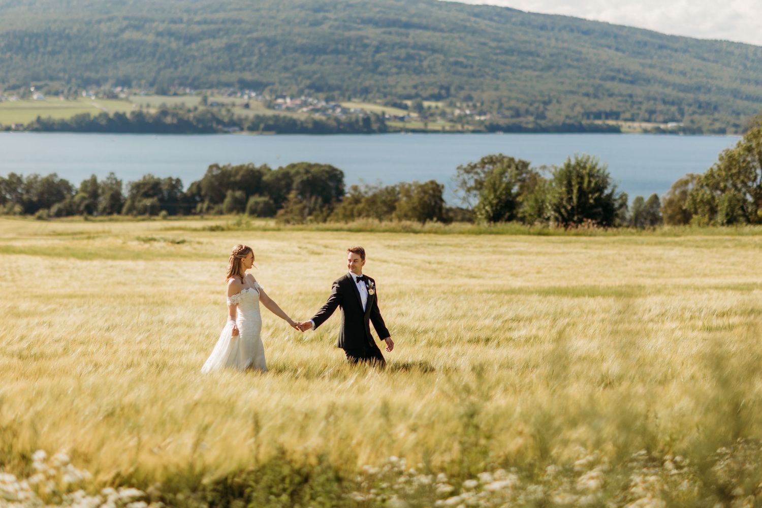 Wedding couple poses in golden wheat field with mountain landscape in background.