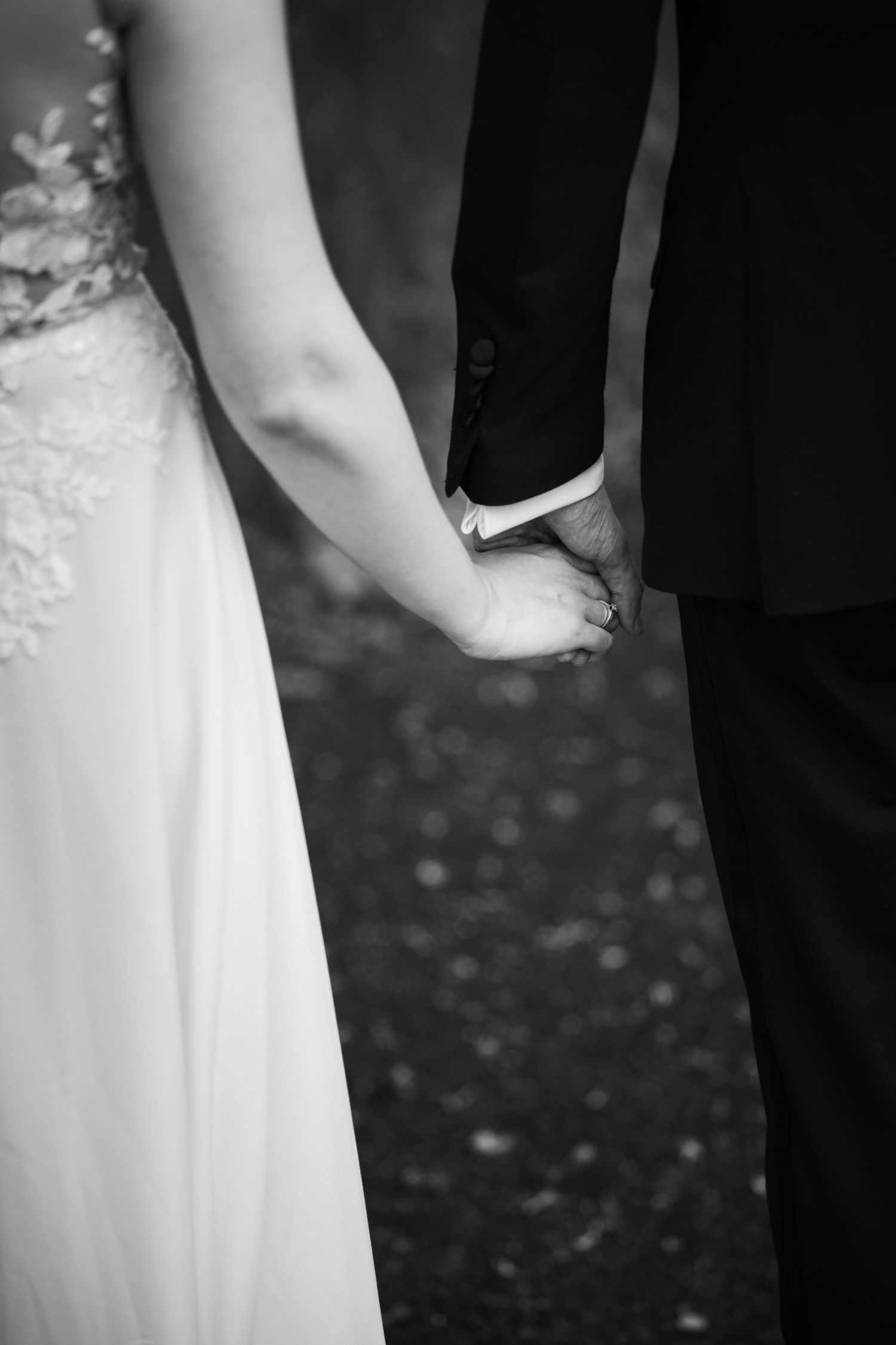 Black and white detail shot of wedding couple's hands and dress.
