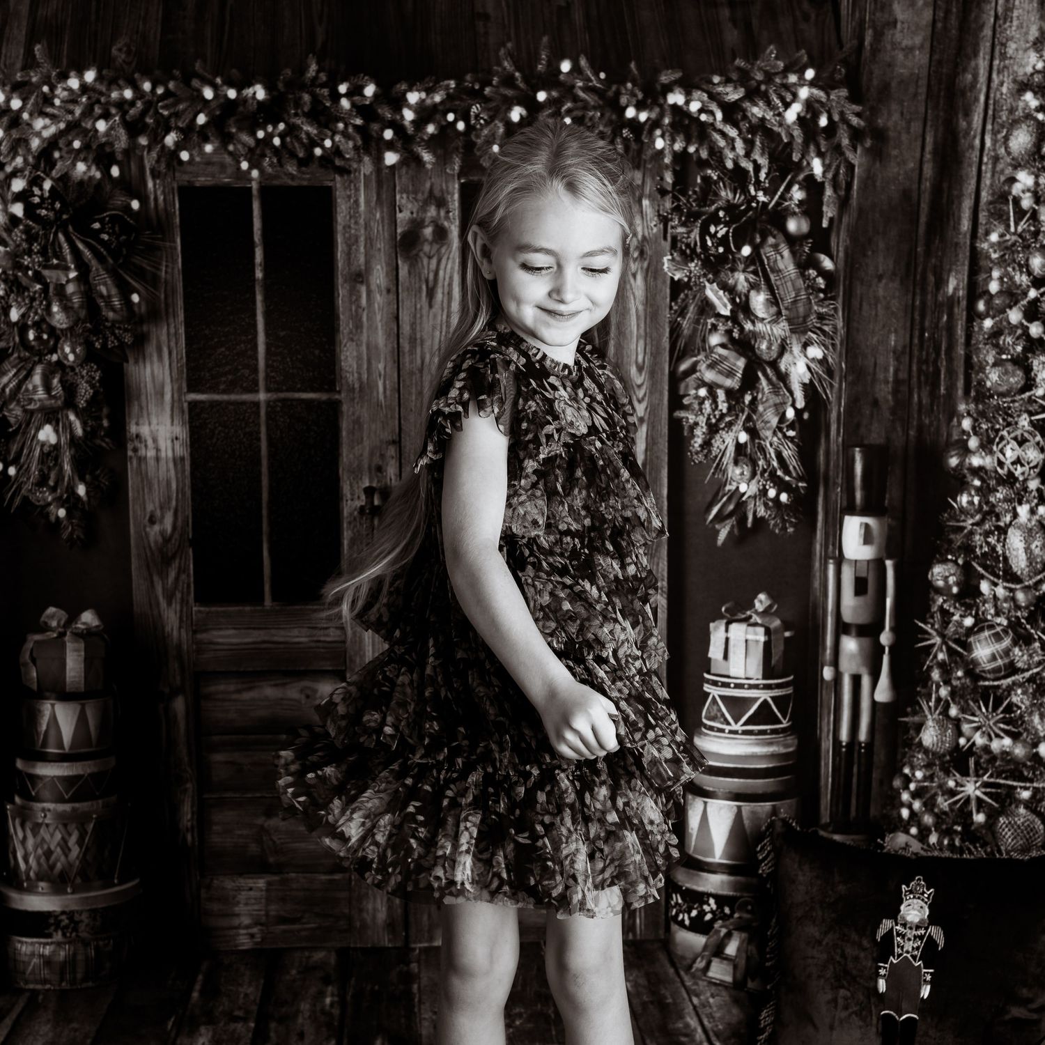 Artistic black and white portrait showing joyful movement against a rustic wooden backdrop with holiday decor.