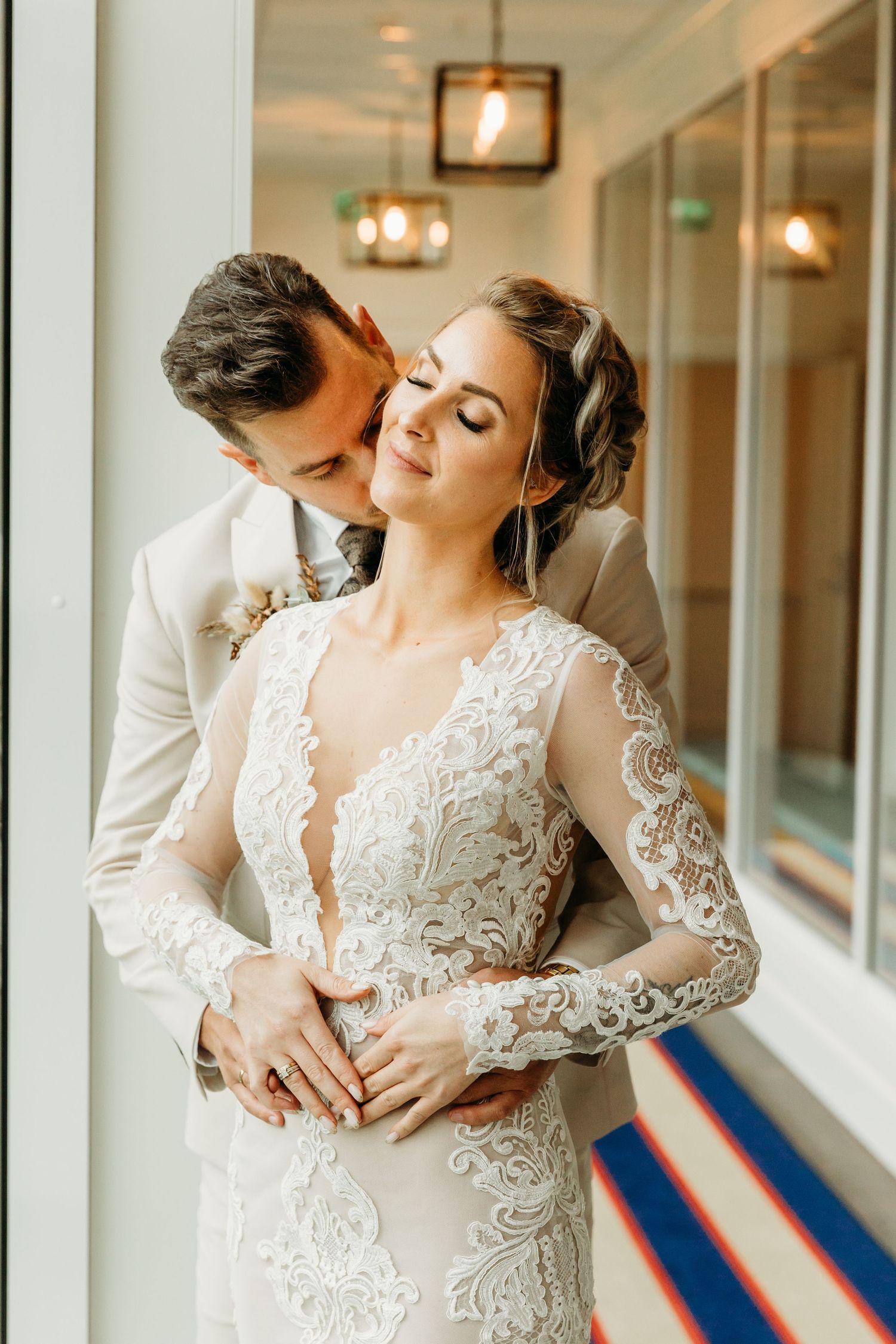 Romantic wedding couple embraces in an elegant hallway with warm lighting and decorative details.