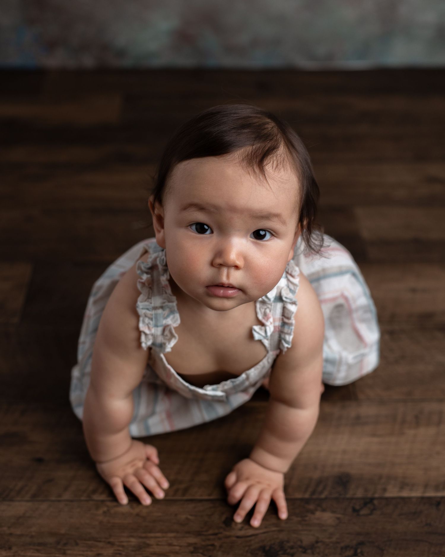 Baby in floral dress crawling on rustic wooden floor during photo session.
