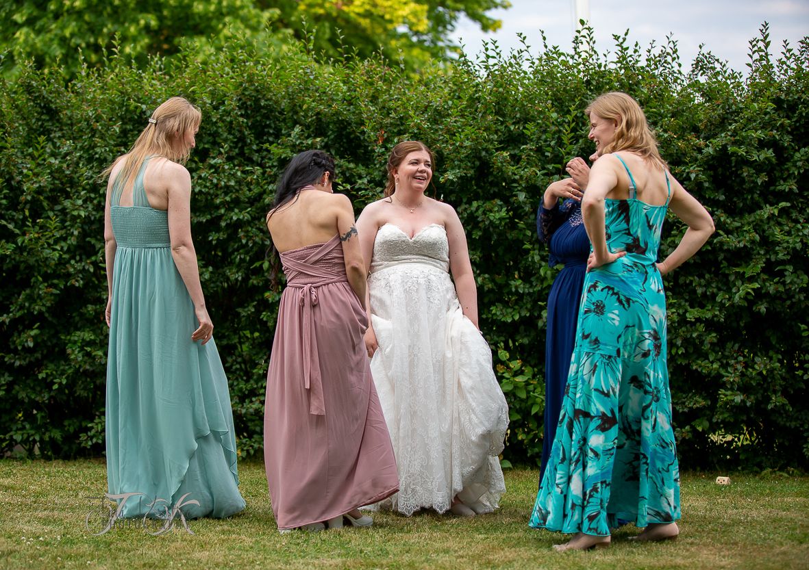 Bridesmaids in colorful floor-length dresses gather with bride in a garden setting.