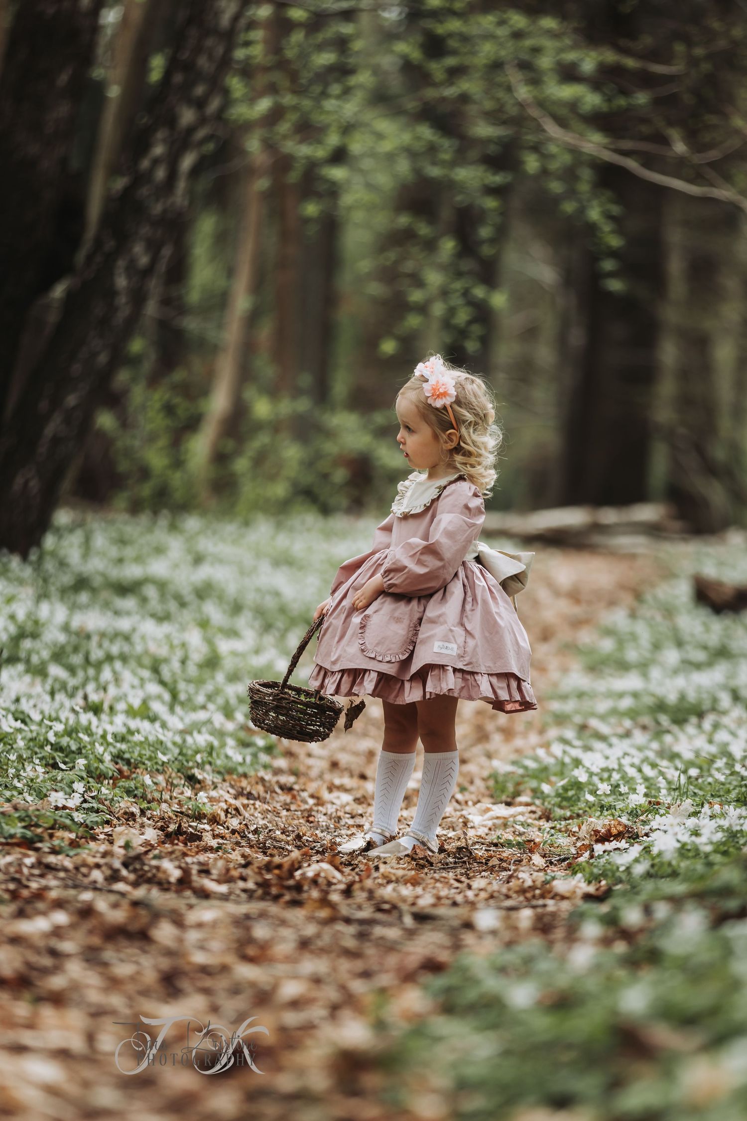 Child in pink dress exploring forest floor covered in white spring flowers.