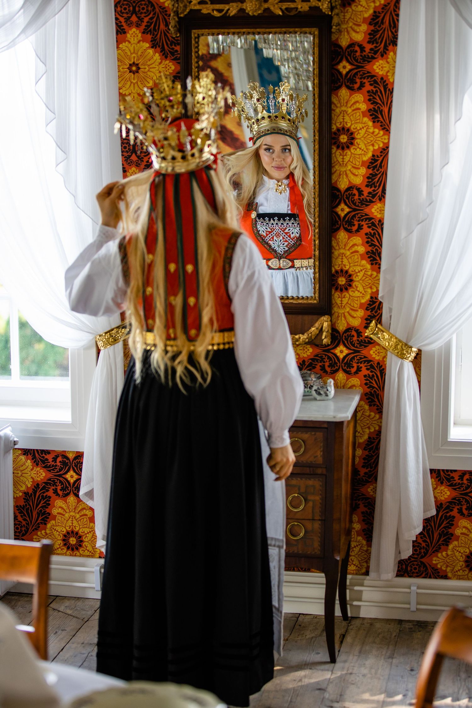 Traditional folk costumes displayed against ornate wallpaper in a bright room.