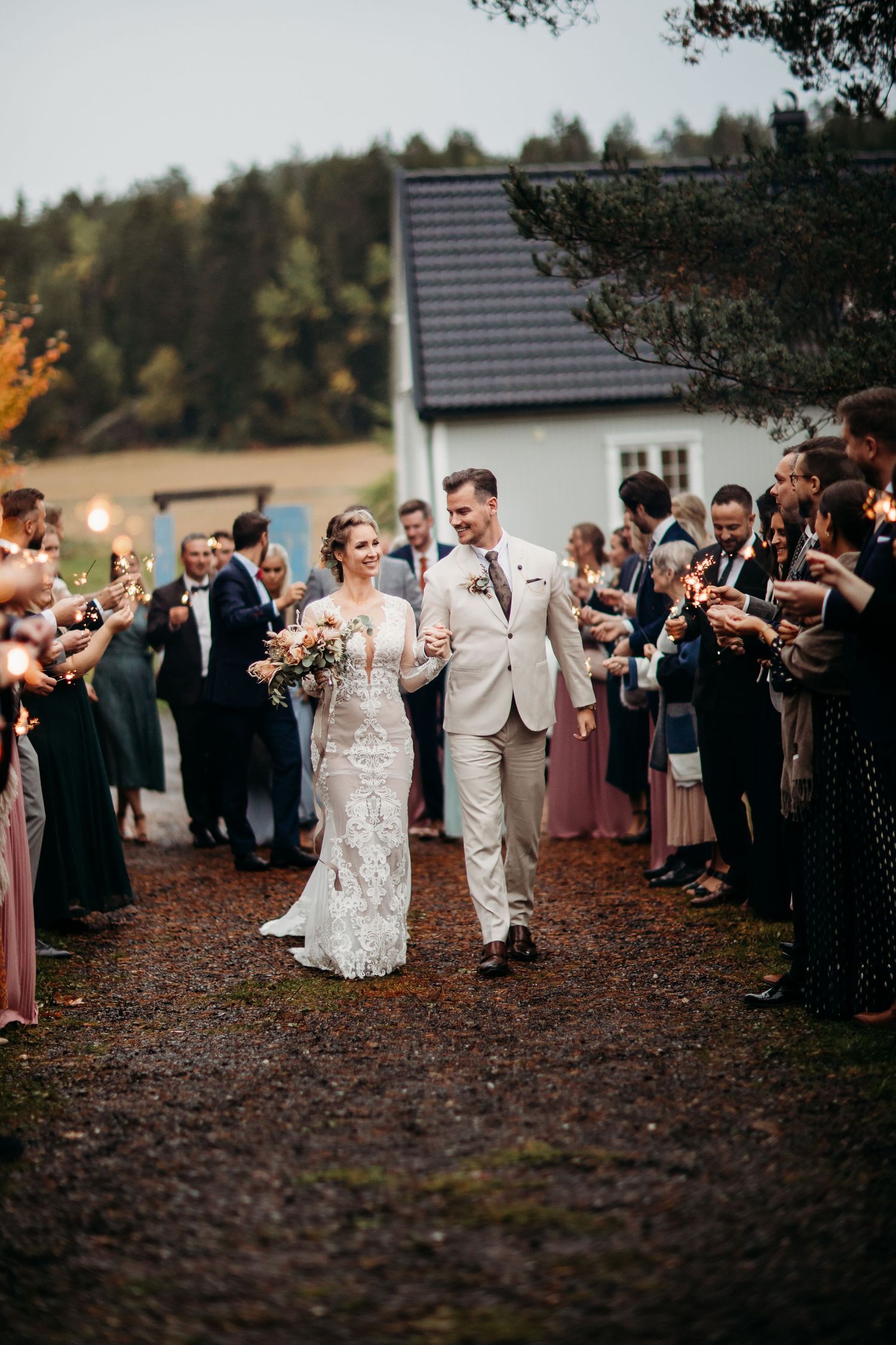 Wedding couple walks through sparkler tunnel lined with guests in formal attire.