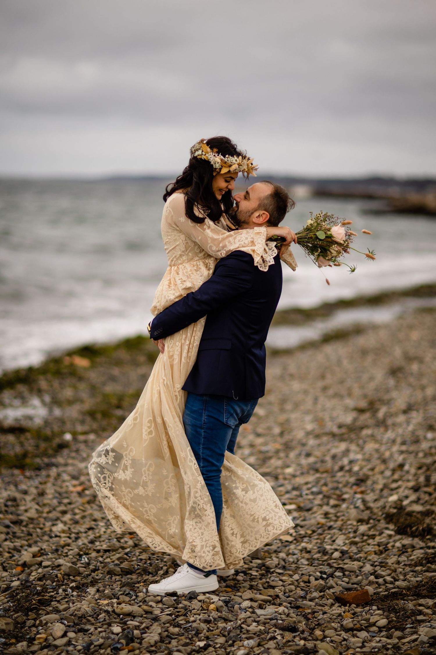 Playful wedding couple dancing and spinning on rocky coastal shoreline.