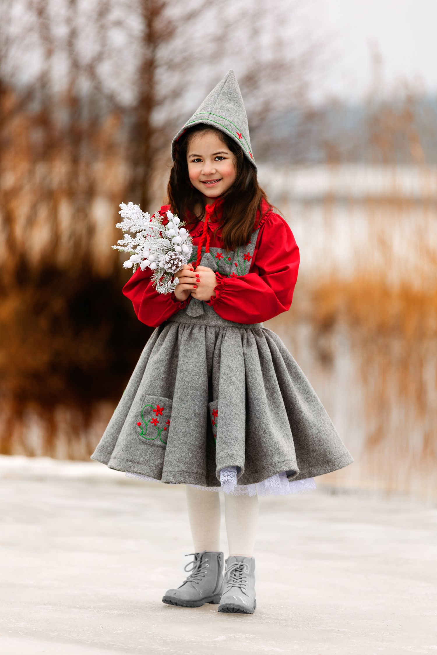 A winter portrait featuring a grey and red dress with matching hat and boots holding a white snowflake decoration.