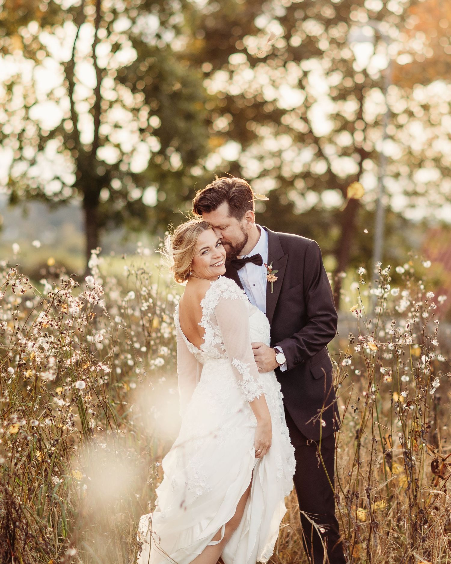 Newlywed couple standing in golden sunlit field with wildflowers.