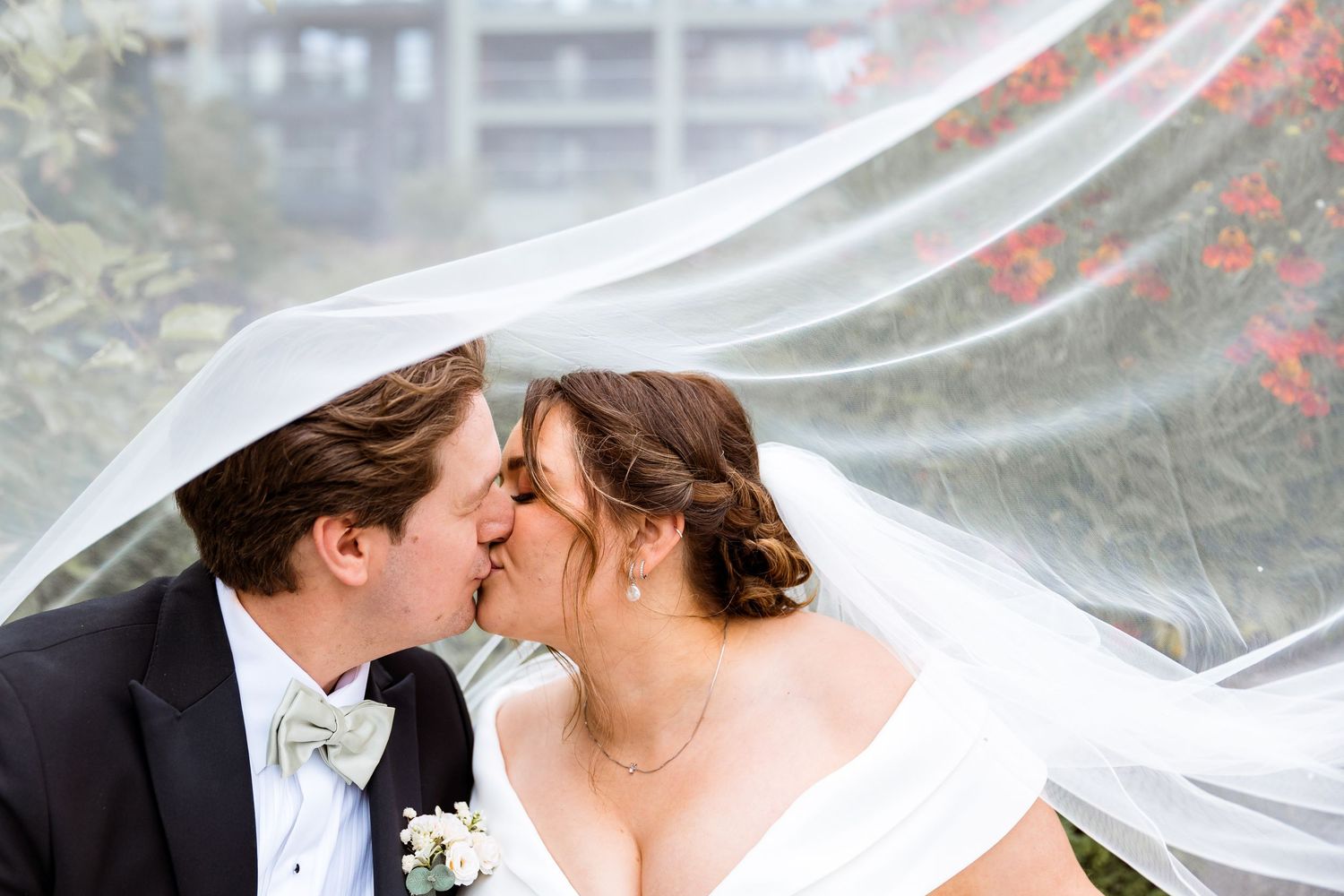 A romantic wedding kiss captured under flowing veil with soft background.