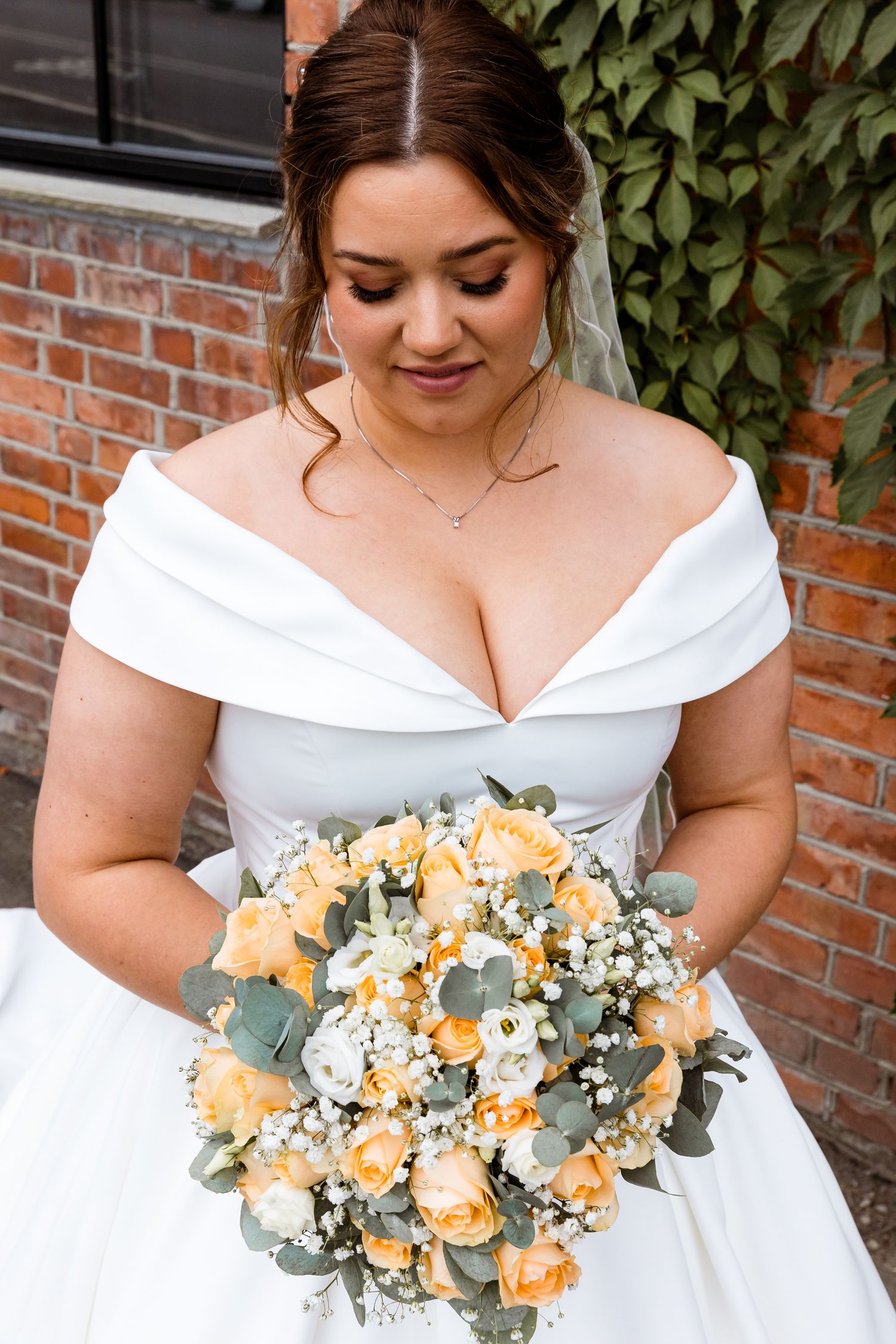 An elegant bridal portrait featuring a beautiful bouquet of peach roses and eucalyptus against brick backdrop.