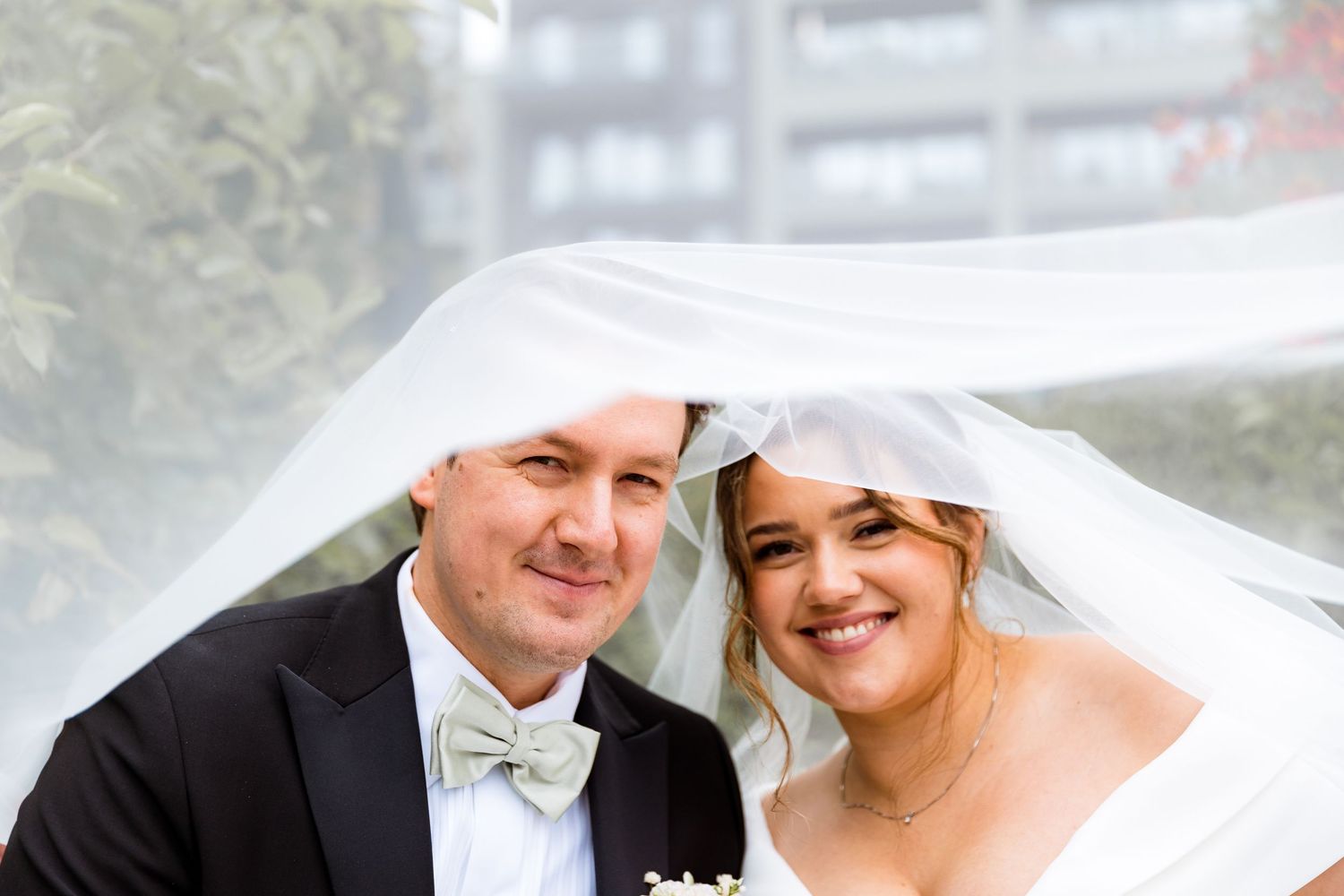 A joyful wedding portrait under flowing veil with soft background.