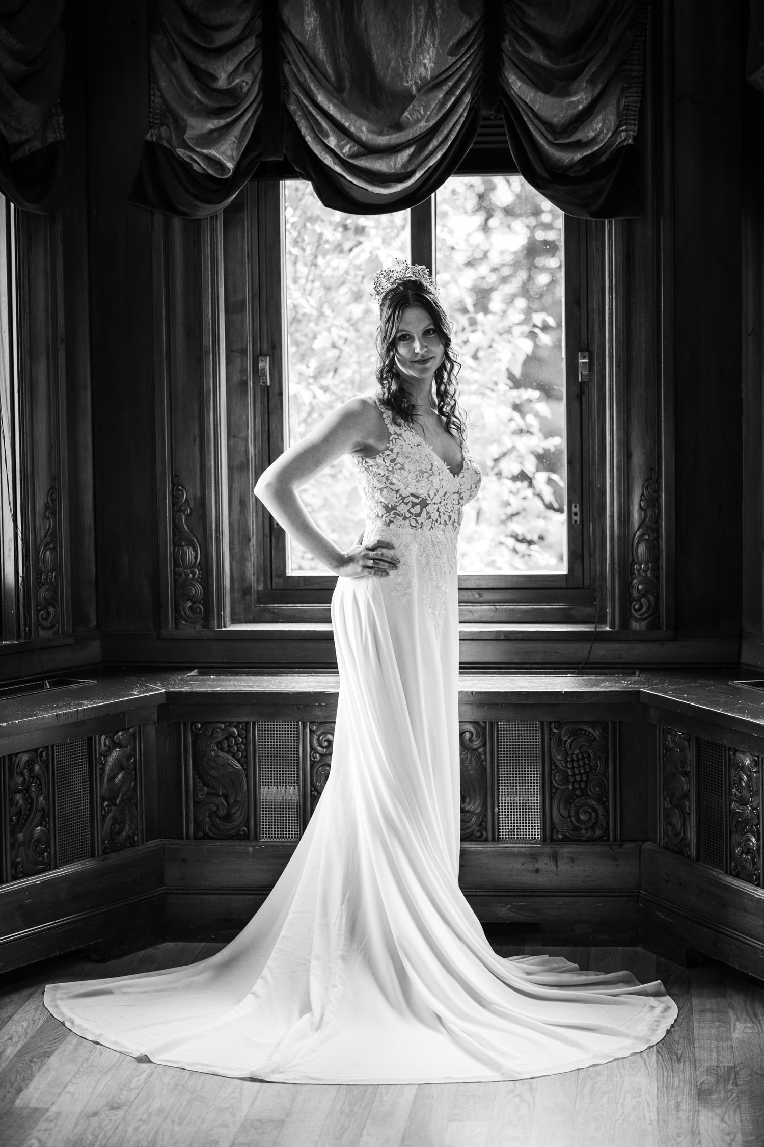 Dramatic black and white photos of a wedding dress with train in a wood-paneled room with natural light.