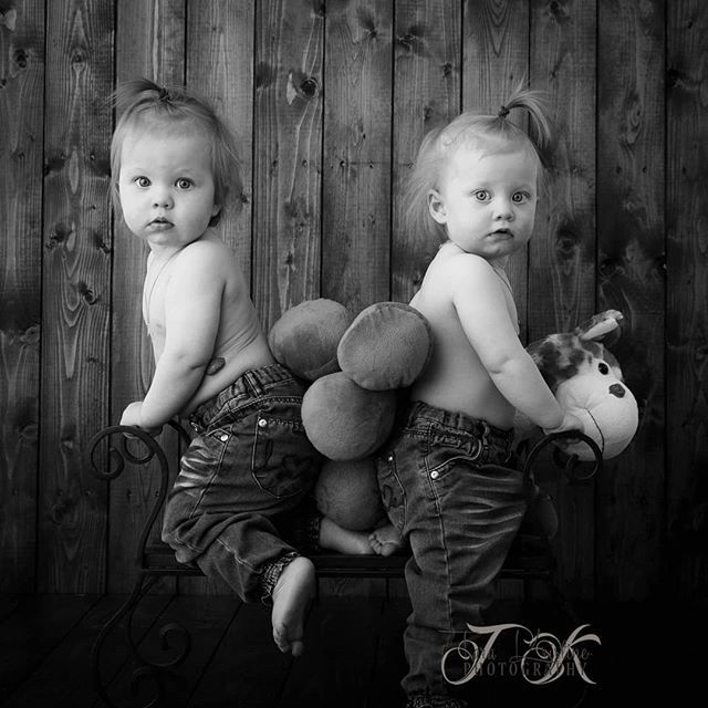 Black and white series of a baby in dark overalls sitting in a wooden bowl against rustic backdrop.