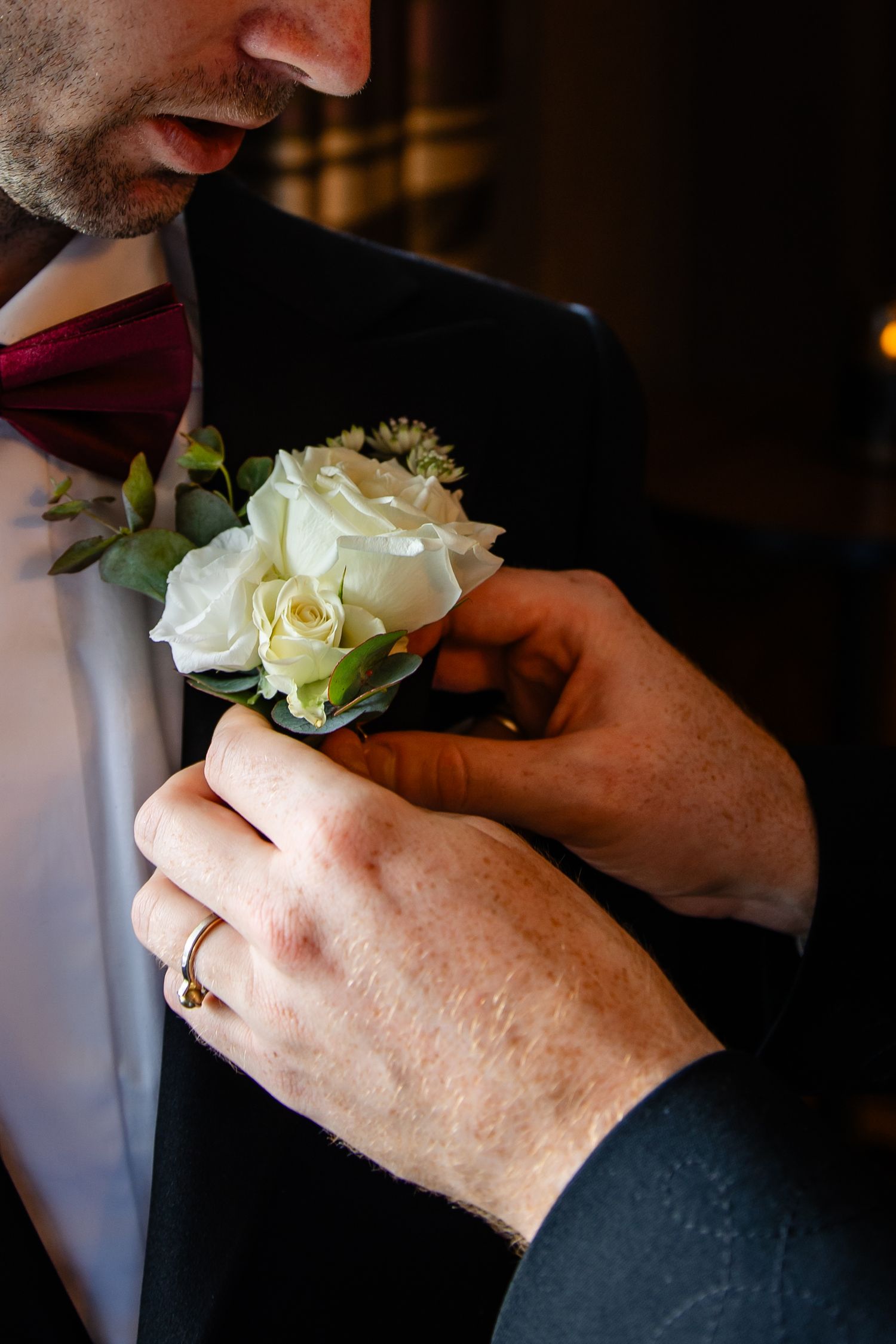 Close-up of hands pinning a white rose boutonniere onto a dark suit jacket.