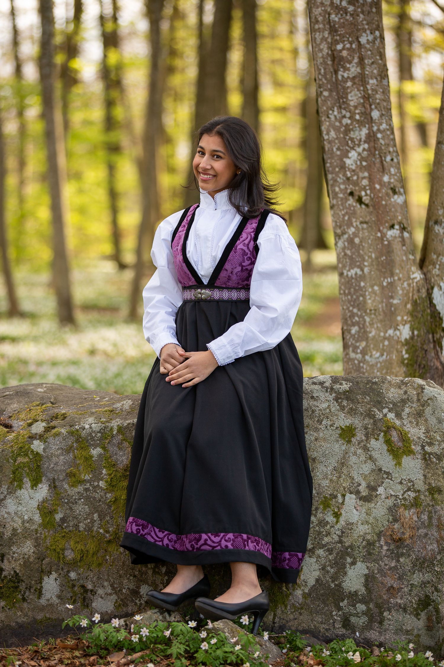 Portrait series in traditional dress sitting on mossy stone wall in forest.