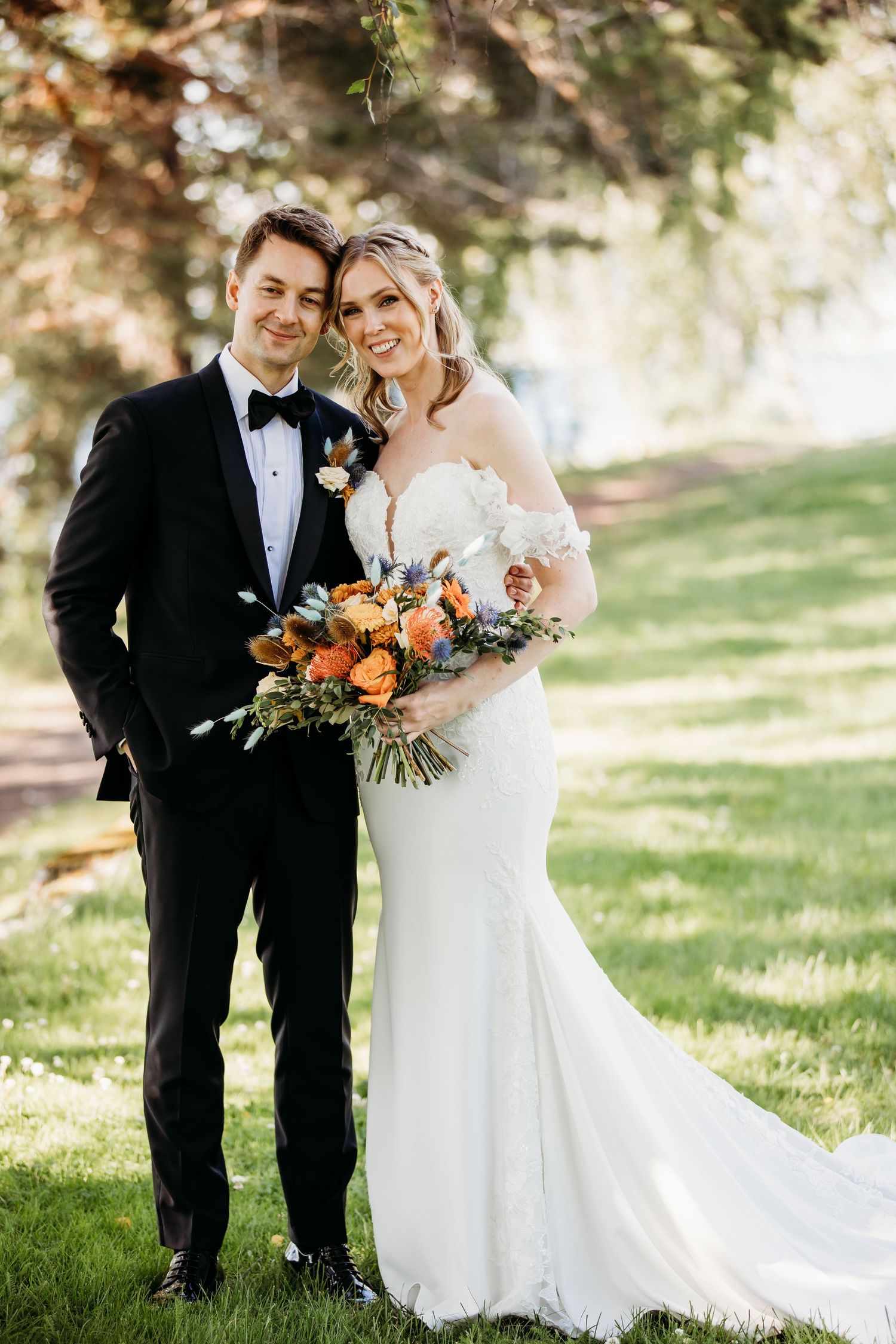 Wedding couple with autumn bouquet featuring orange flowers and greenery.