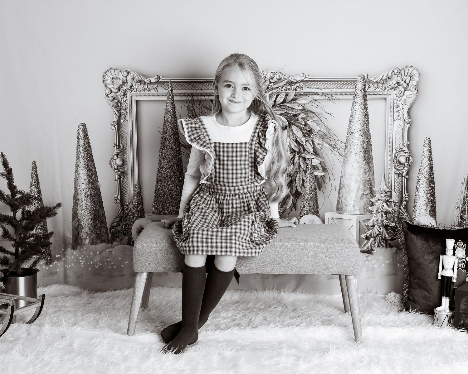 Black and white portrait of a child in a gingham dress sitting in a winter wonderland themed studio setting.