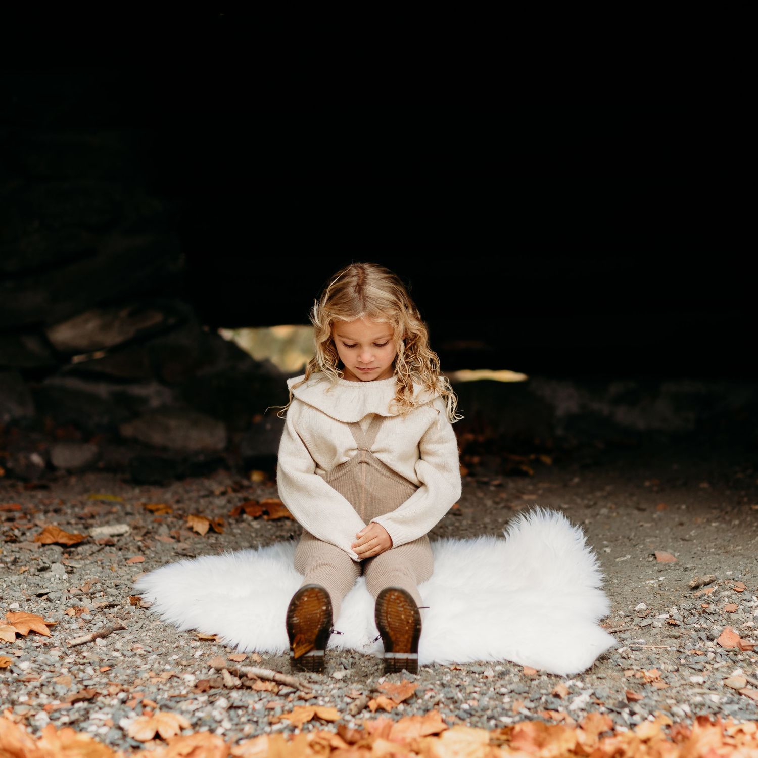 Person sitting on white fur rug with autumn leaves scattered nearby.