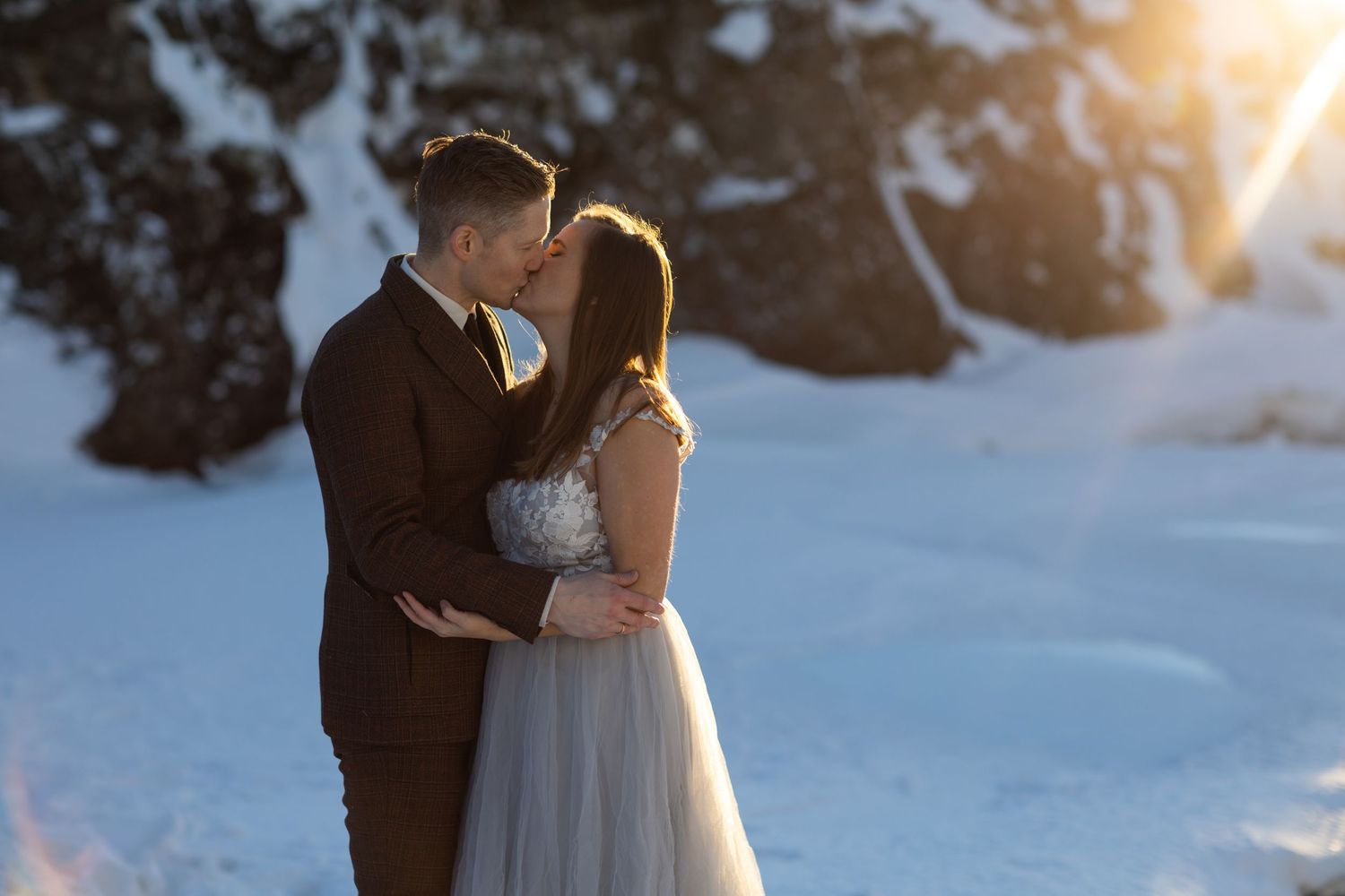 Romantic winter wedding portrait with couple silhouetted against snowy backdrop.
